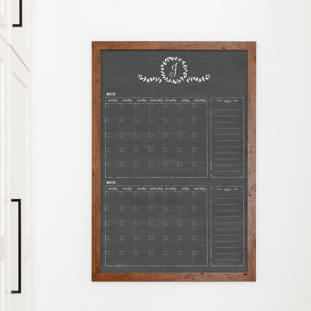 A framed chalkboard dry-erase calendar with a two month design format hanging on the wall