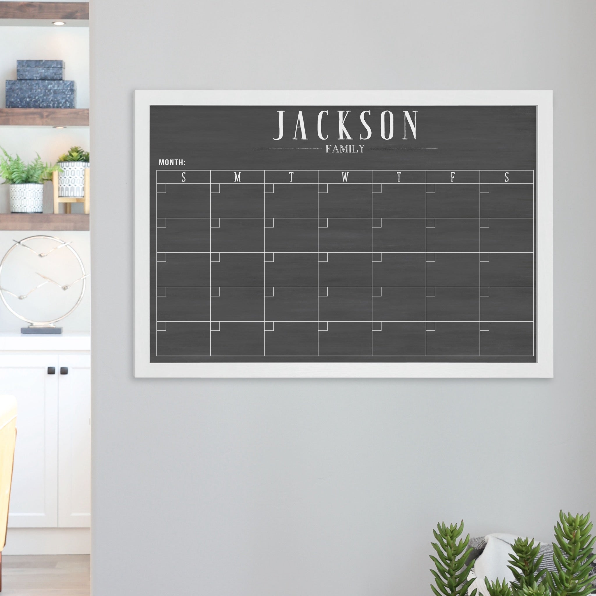 A framed dry-erase monthly calender with a chalkboard look hanging on the wall