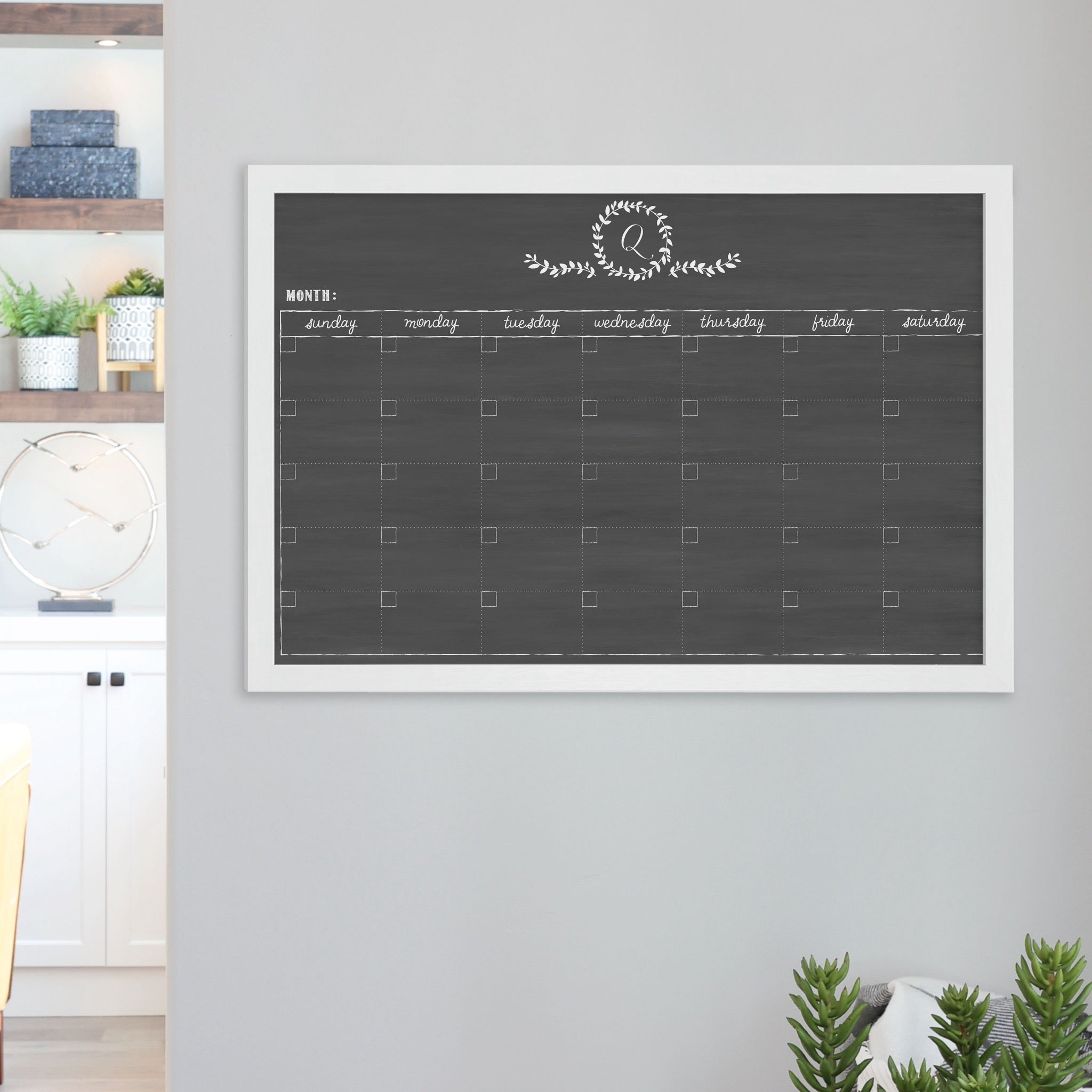A framed dry-erase monthly calender with a chalkboard look hanging on the wall