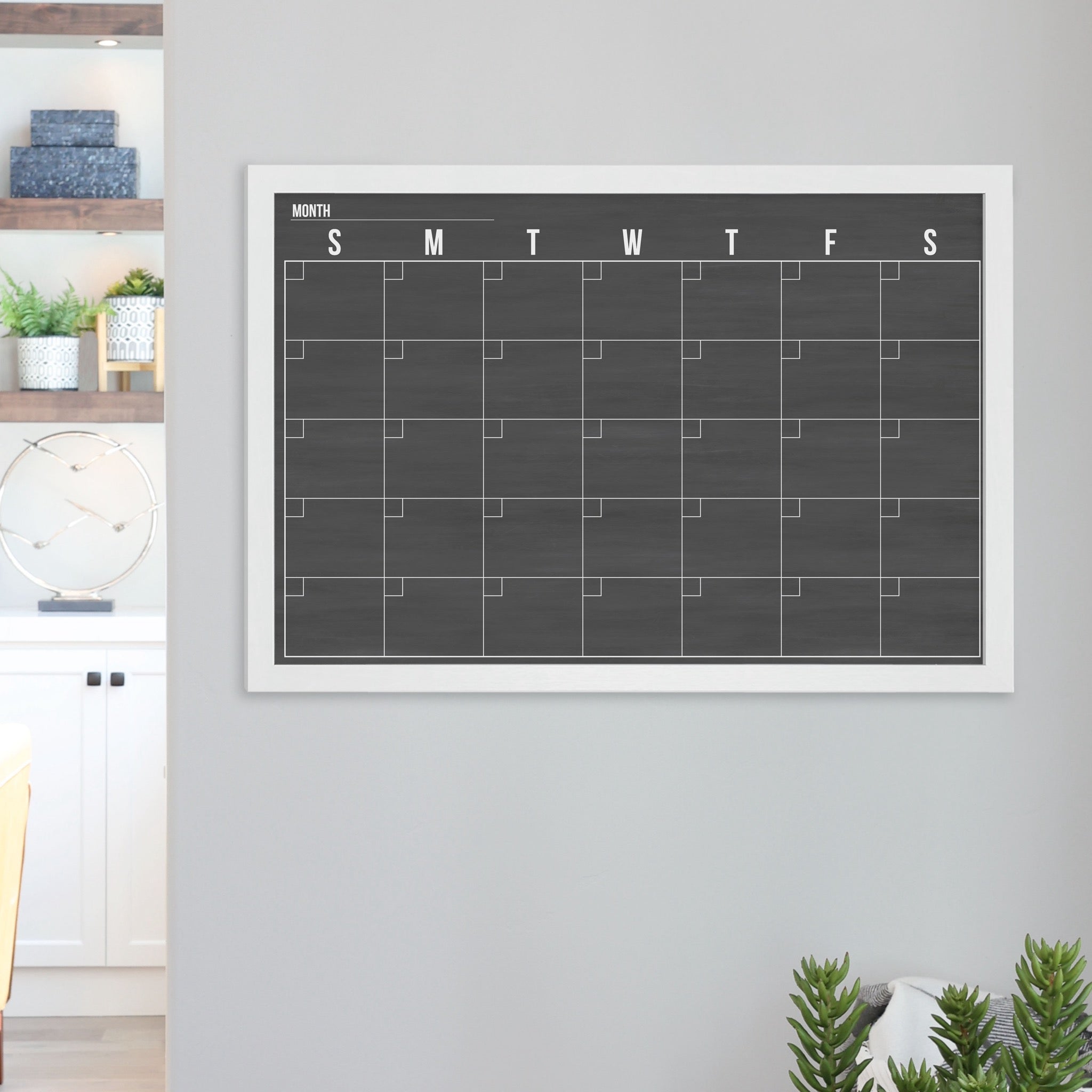 A framed dry-erase monthly calender with a chalkboard look hanging on the wall