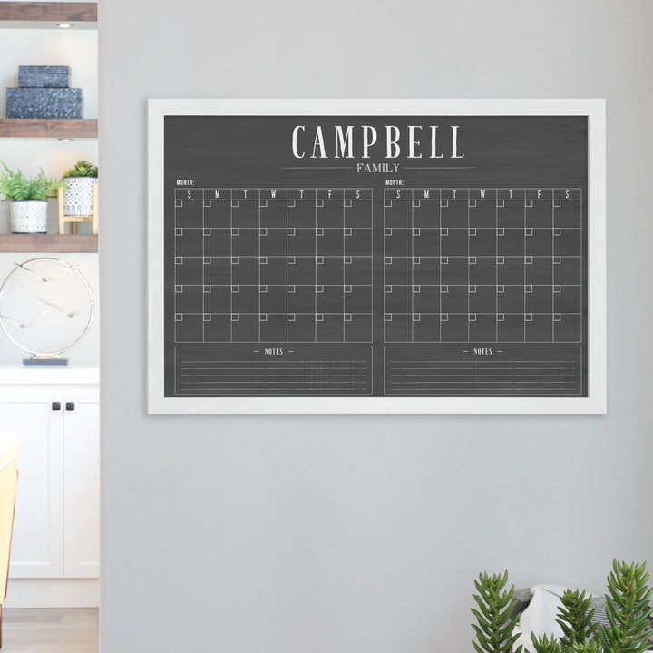 A framed chalkboard dry-erase calendar with a two month design format hanging on the wall