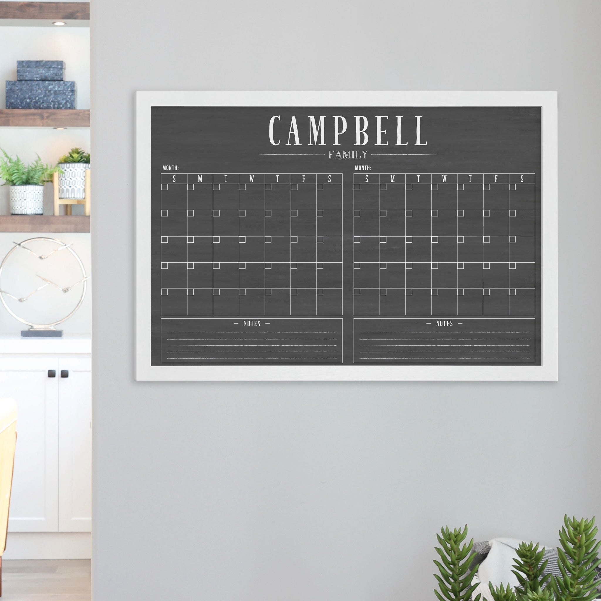 A framed chalkboard dry-erase calendar with a two month design format hanging on the wall
