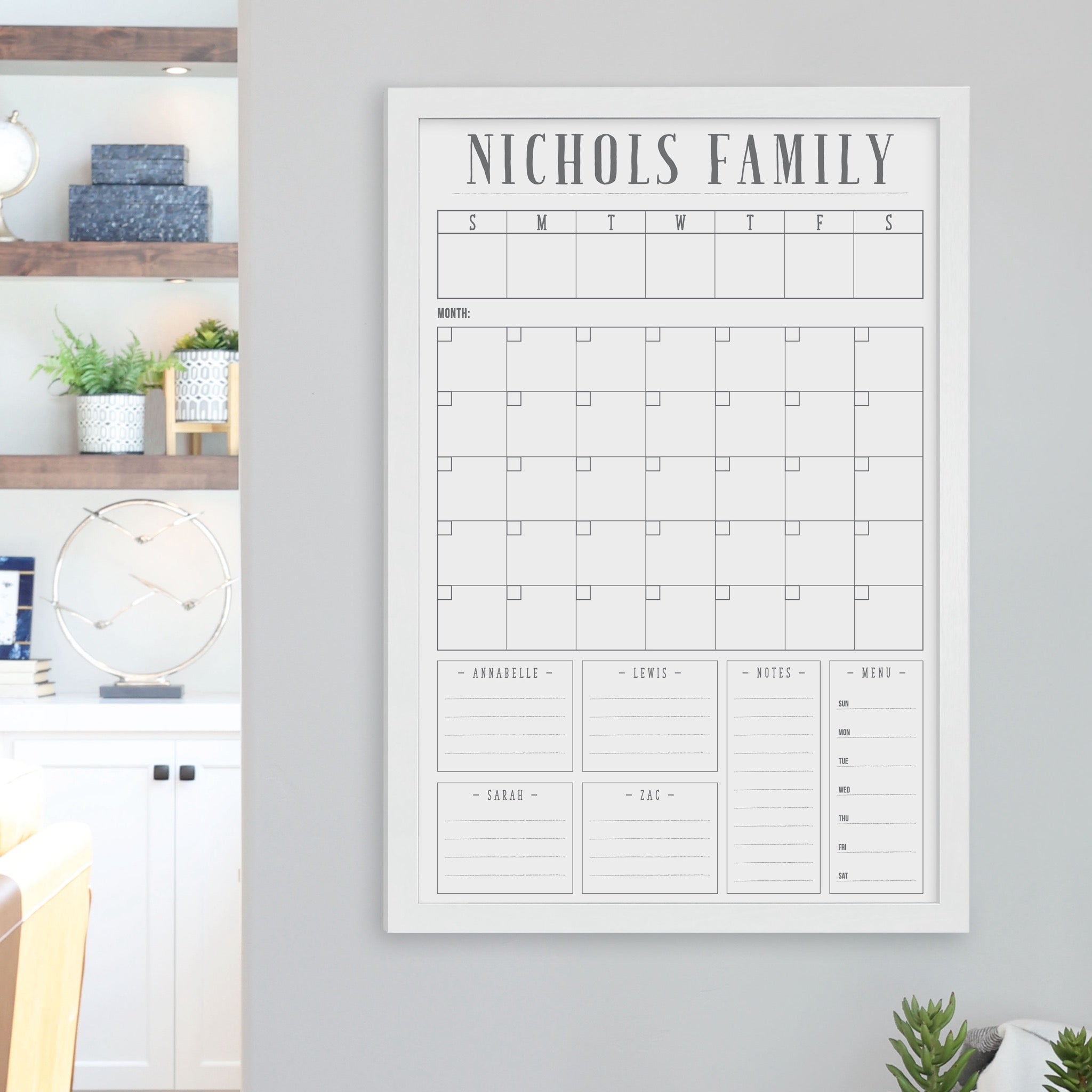 A framed whiteboard calendar with a monthly and weekly format hanging on the wall