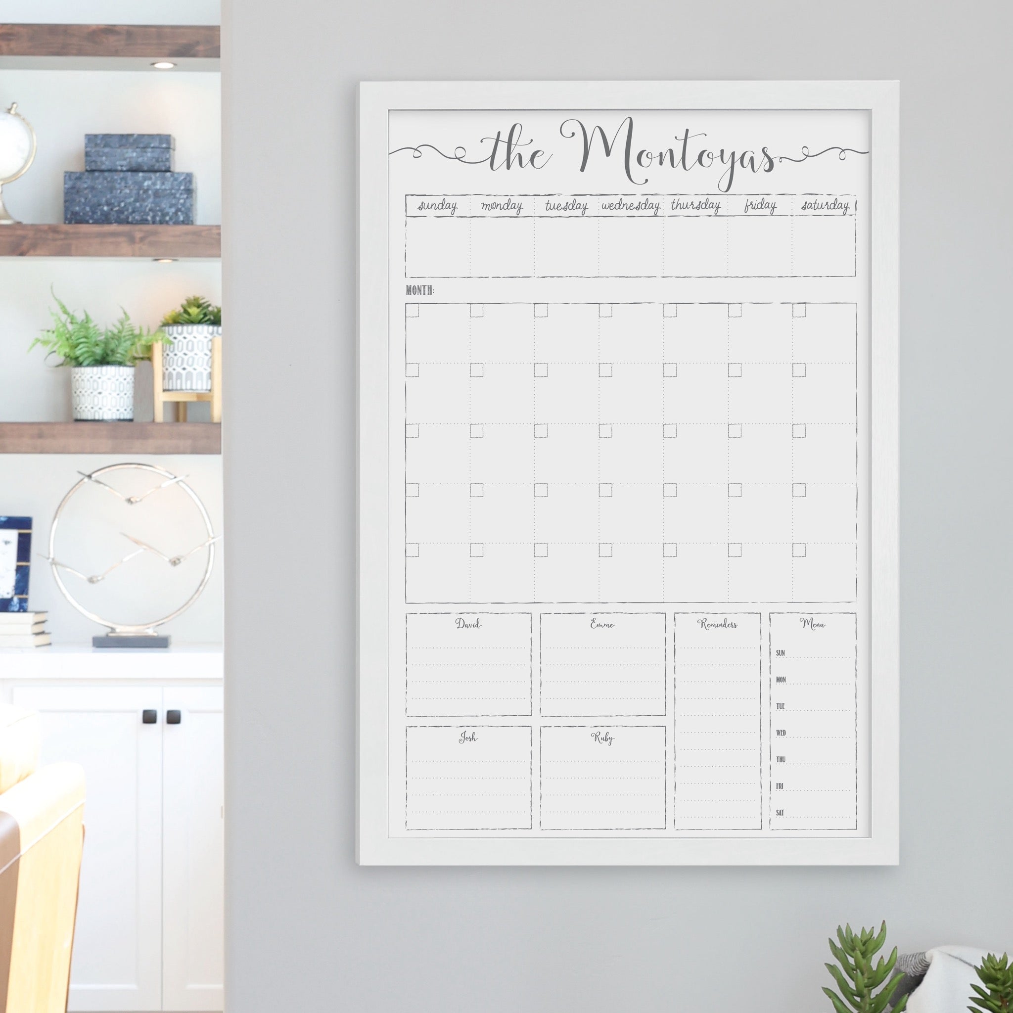 A framed whiteboard calendar with a monthly and weekly format hanging on the wall