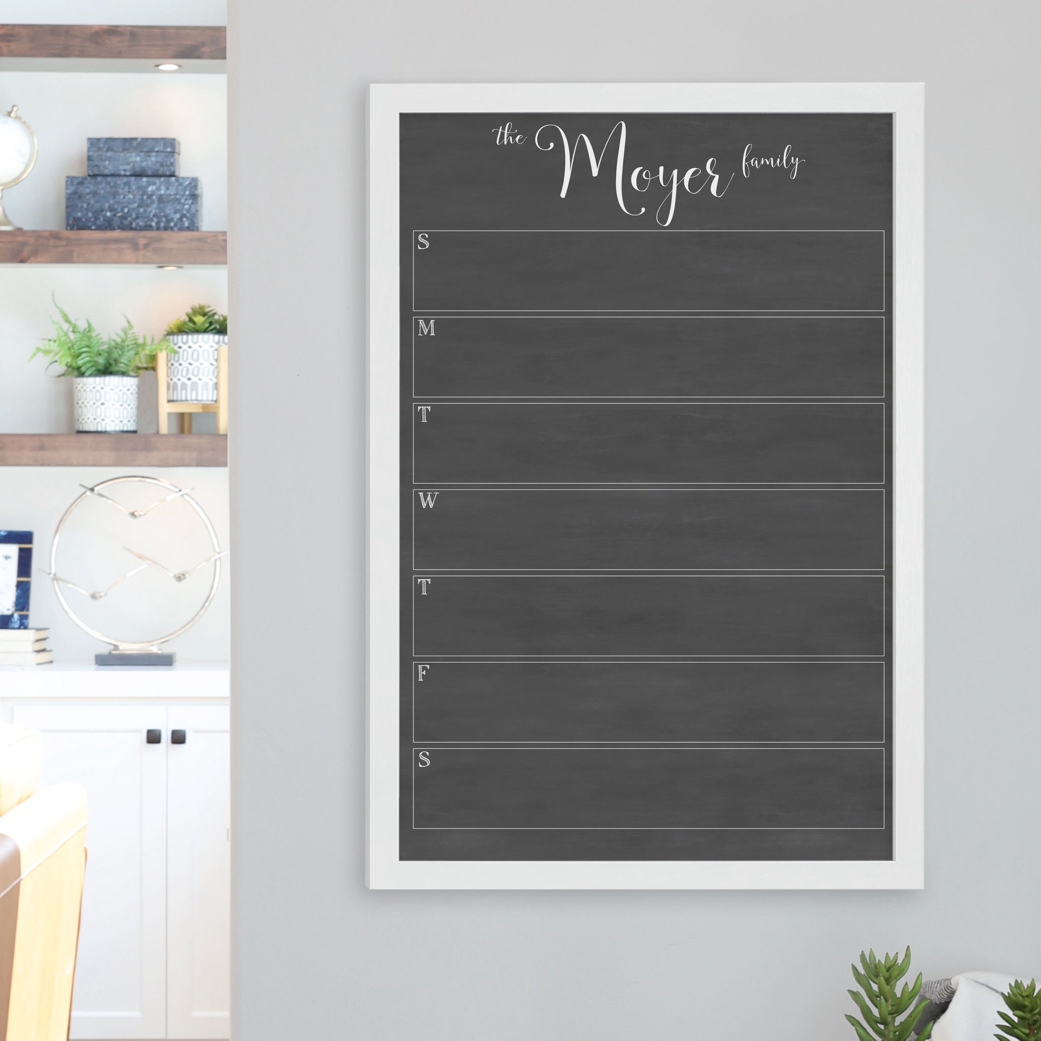 A framed dry-erase weekly calender with a chalkboard look hanging on the wall
