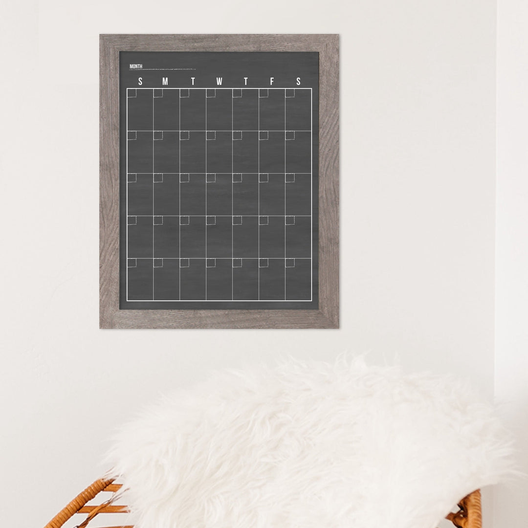 A framed dry-erase monthly calender with a chalkboard look hanging on the wall