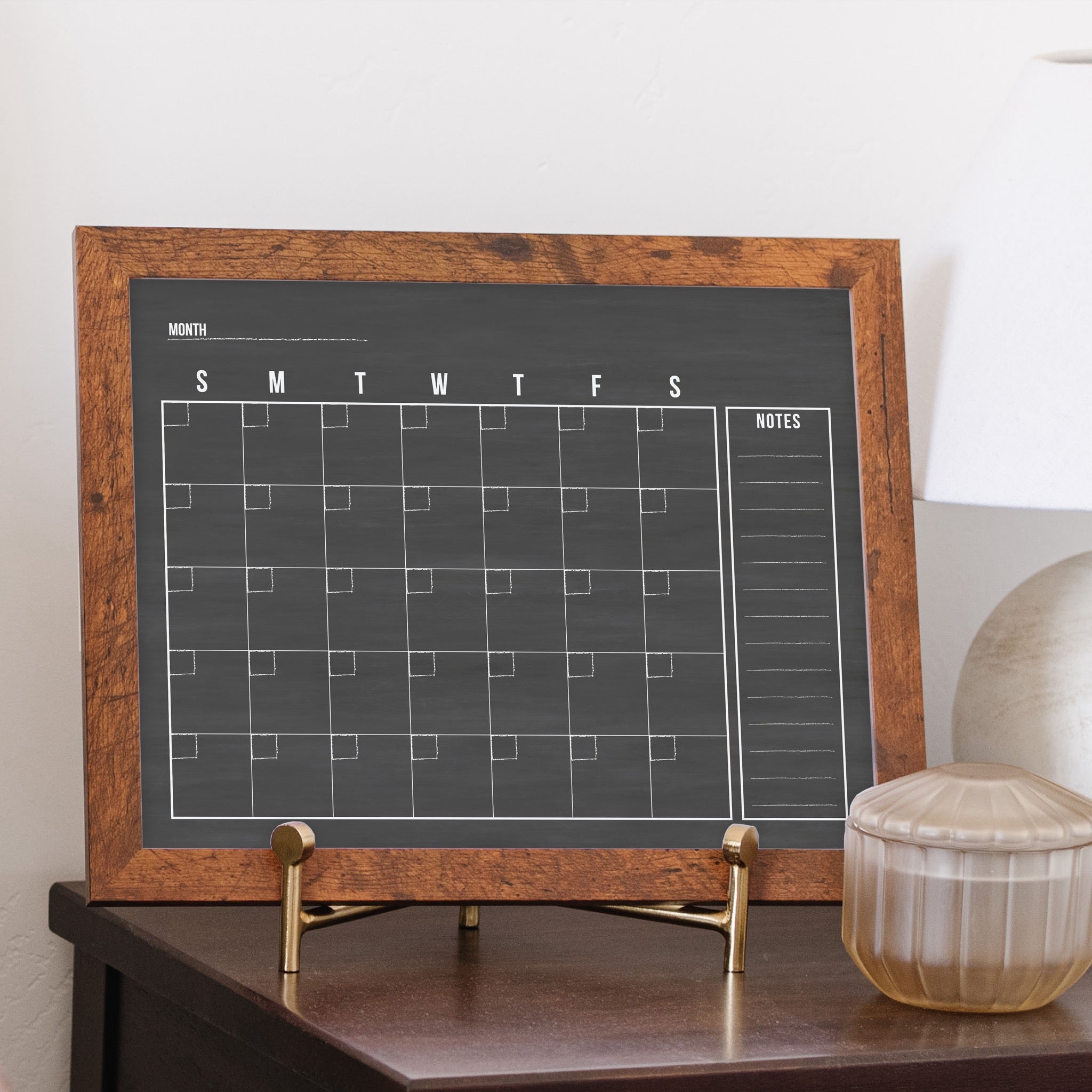 A framed dry-erase monthly calender with a chalkboard look hanging on the wall