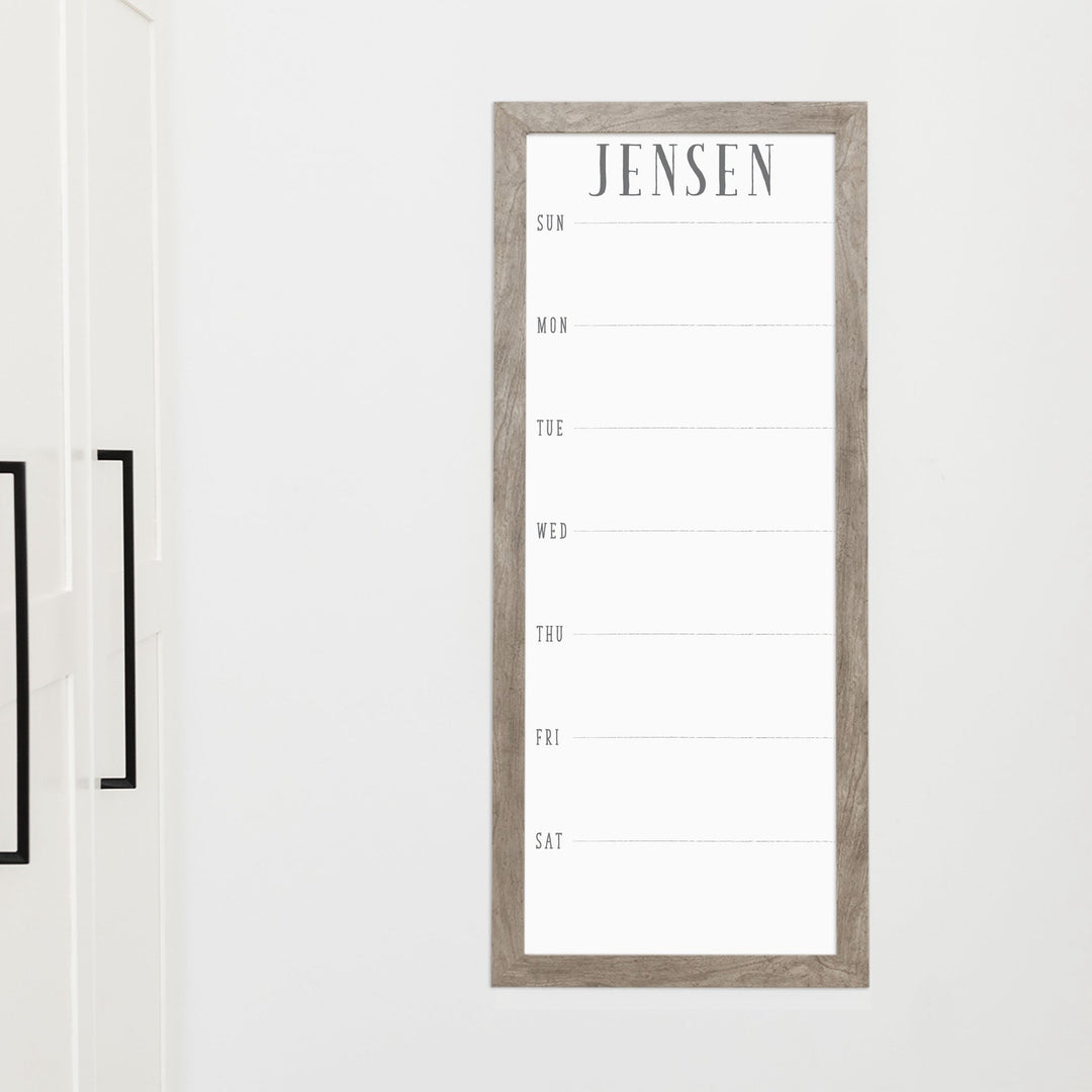 A framed slim whiteboard weekly calender hanging on the wall