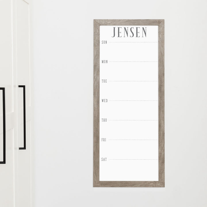 A framed slim whiteboard weekly calender hanging on the wall