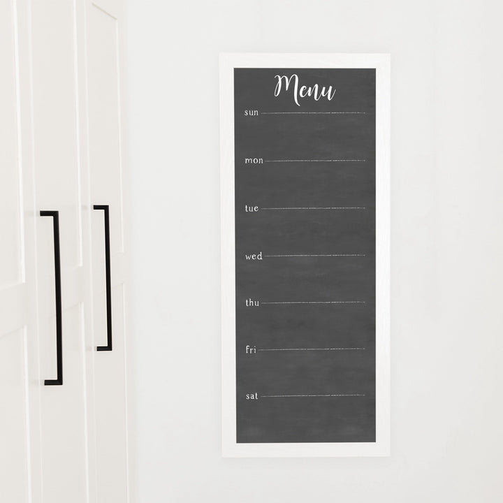 A framed slim dry-erase weekly calender with a faux chalkboard look hanging on the wall