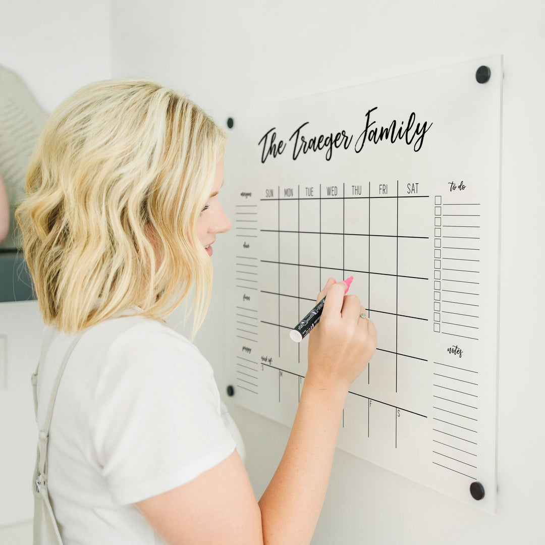 A Dry-erase calendar with a monthly and weekly format made of acrylic hanging on the wall