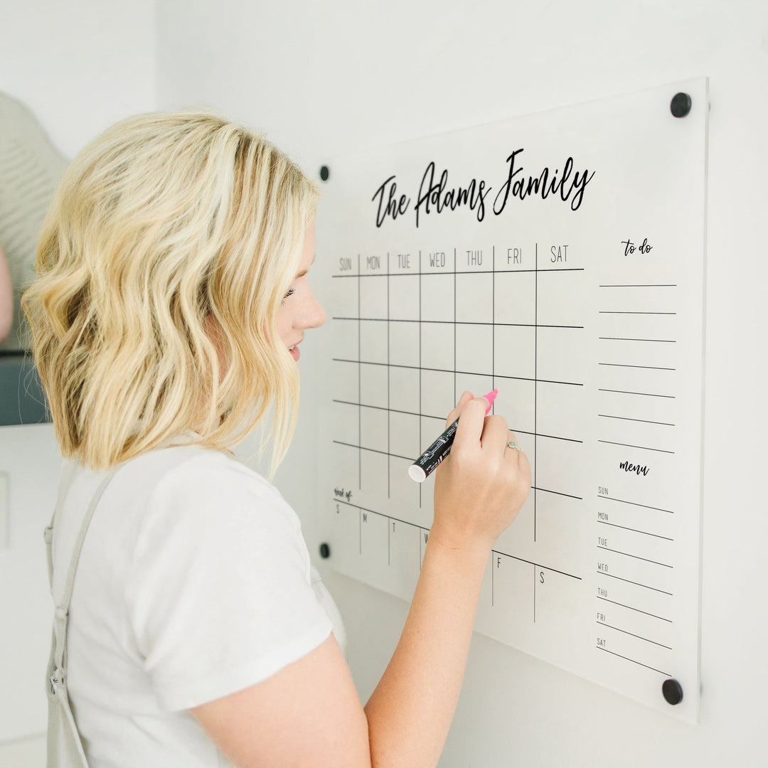 A Dry-erase calendar with a monthly and weekly format made of acrylic hanging on the wall