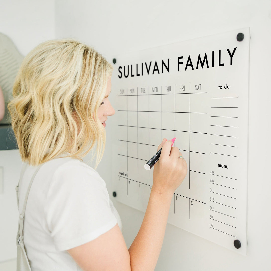 A Dry-erase calendar with a monthly and weekly format made of acrylic hanging on the wall