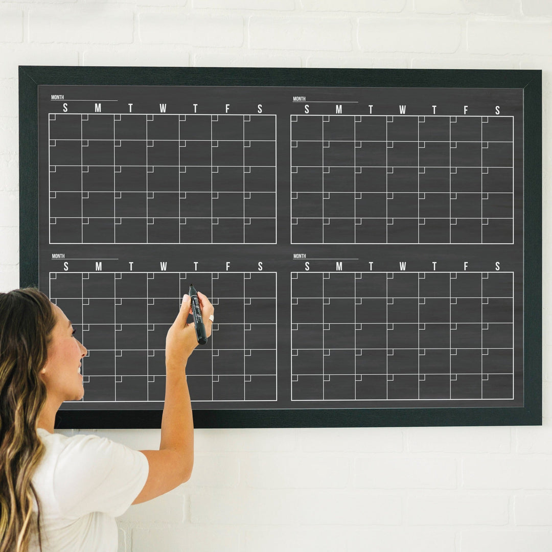 A framed dry-erase four month calendar with a chalkboard look hanging on the wall
