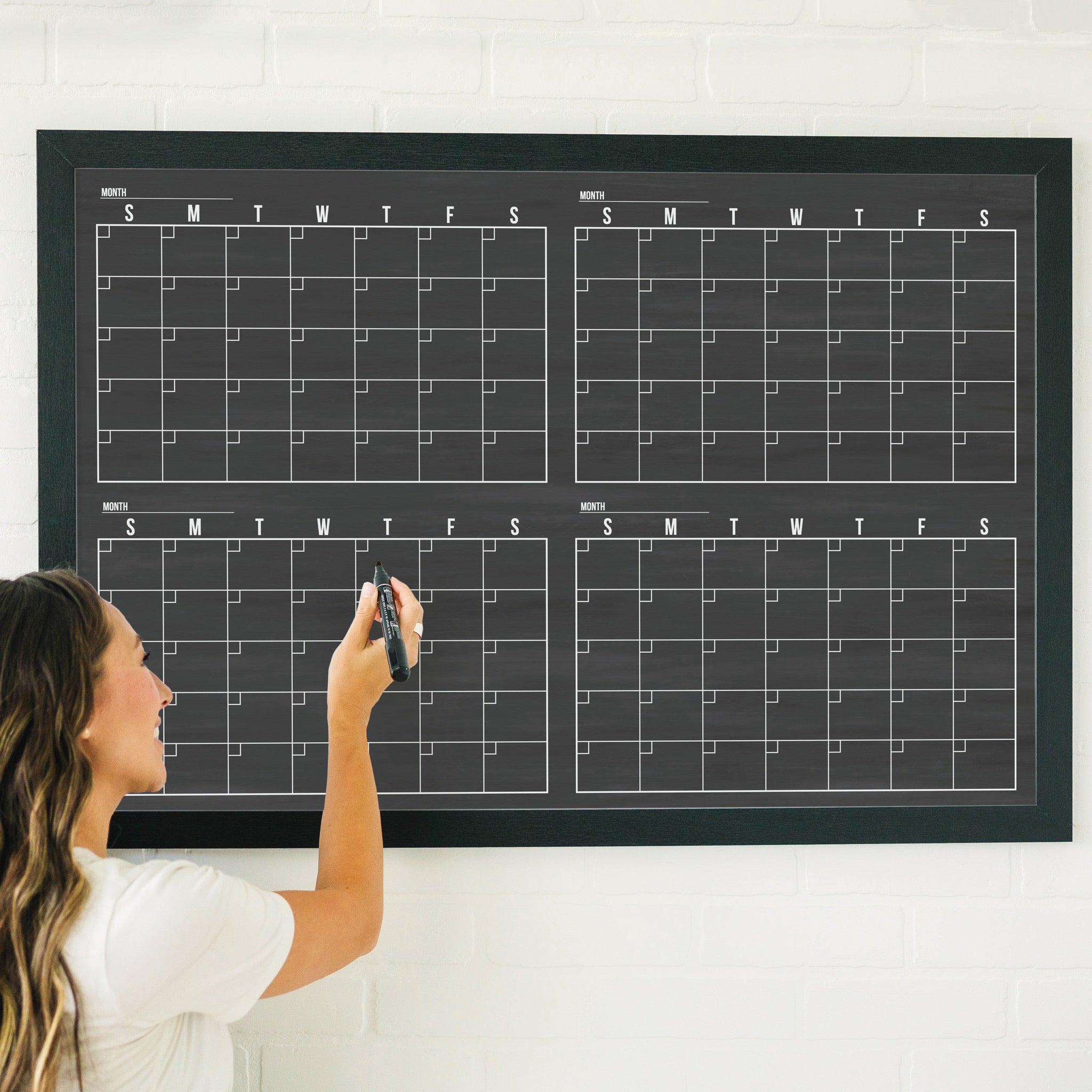 A framed dry-erase four month calendar with a chalkboard look hanging on the wall