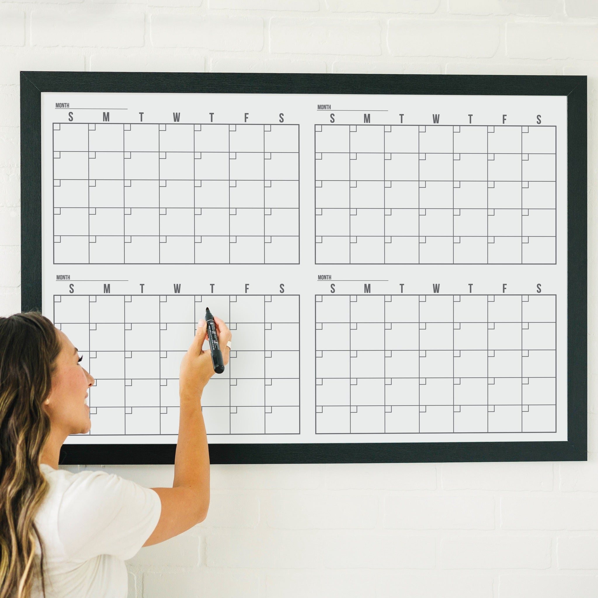 A framed whiteboard four month calendar hanging on the wall