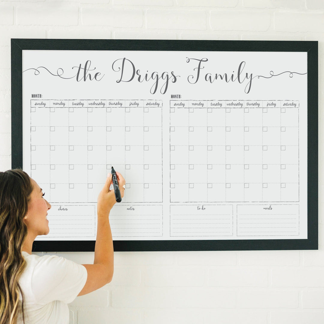 A framed whiteboard calendar with a two month design format hanging on the wall