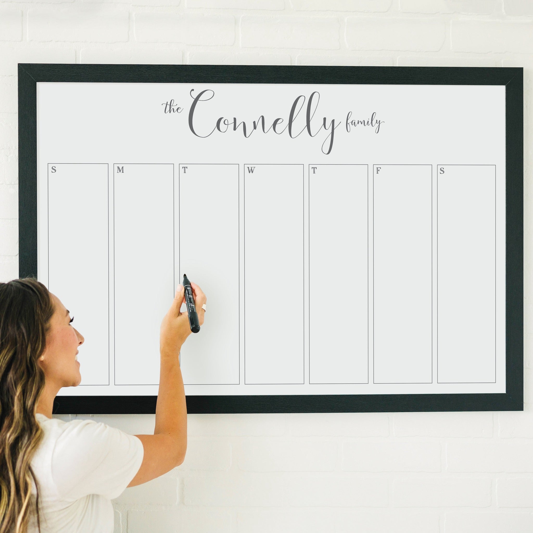 A framed whiteboard weekly calender hanging on the wall
