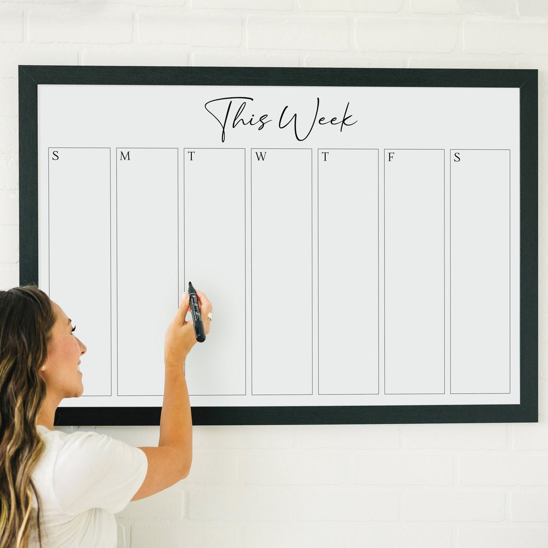 A framed whiteboard weekly calender hanging on the wall