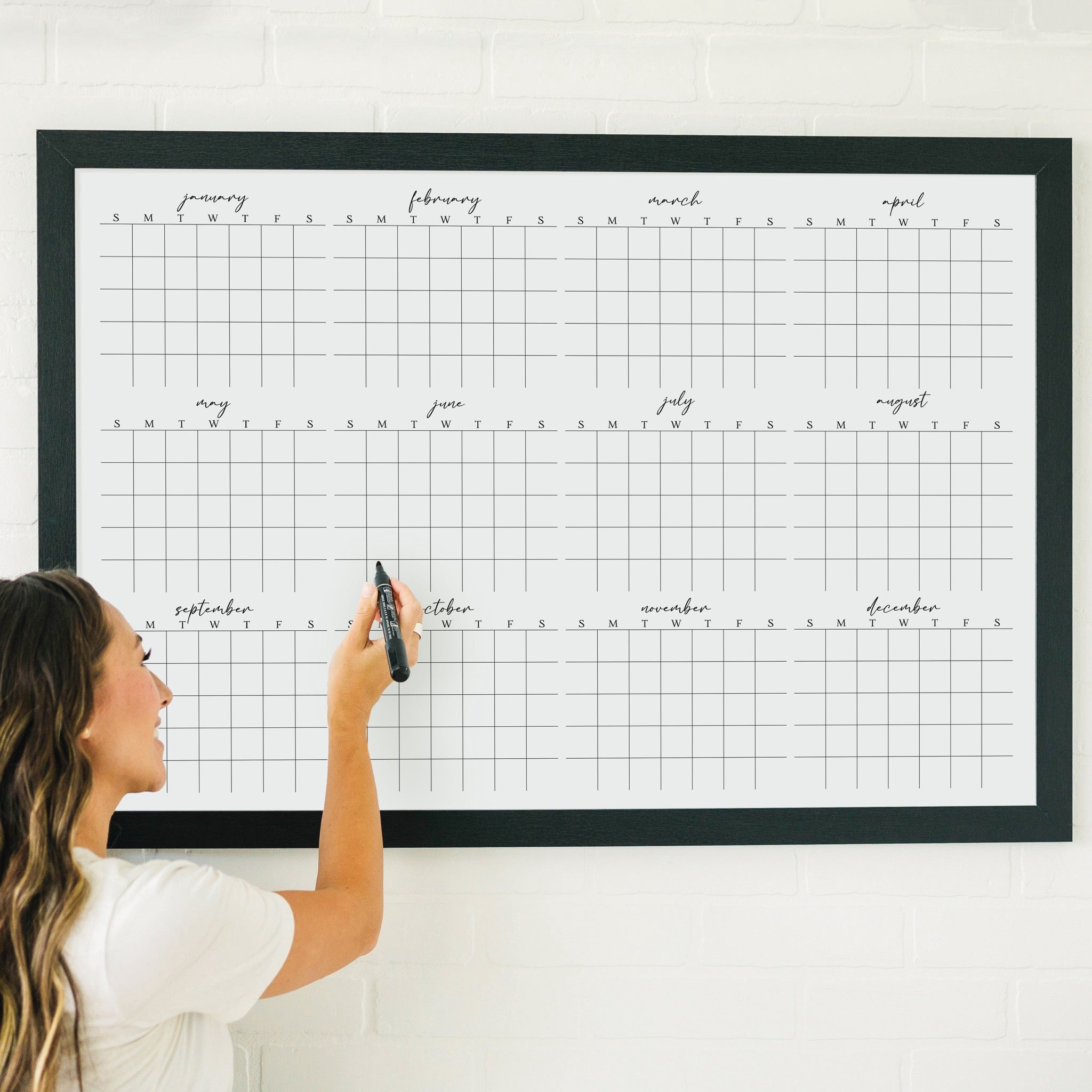 A framed whiteboard yearly calendar hanging up on the wall