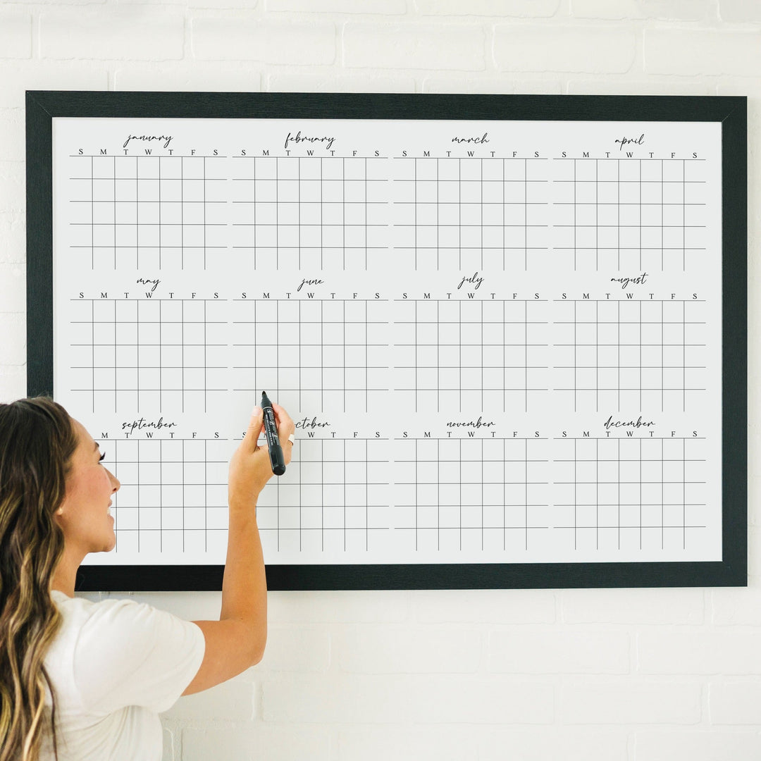 A framed whiteboard yearly calendar hanging up on the wall