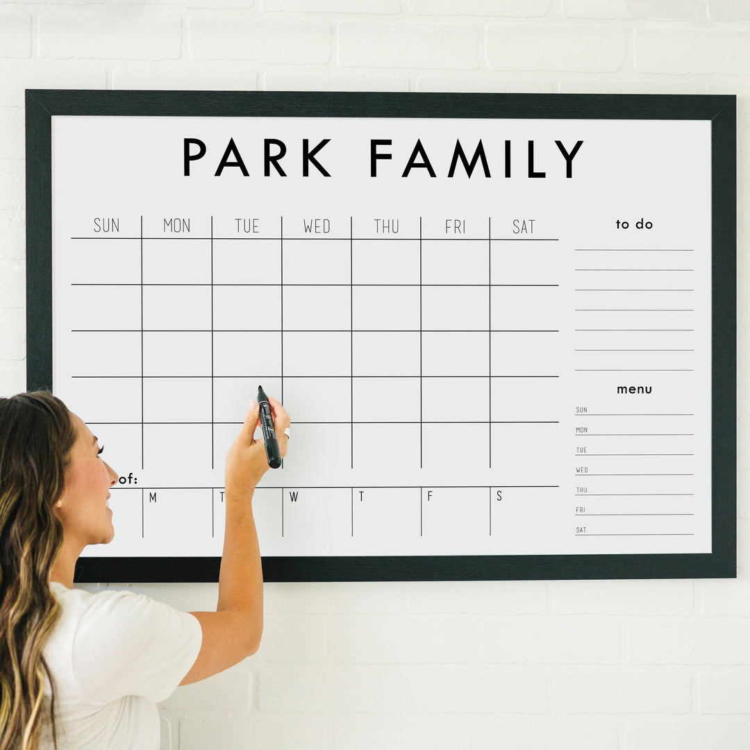 A framed whiteboard weekly calender hanging on the wall
