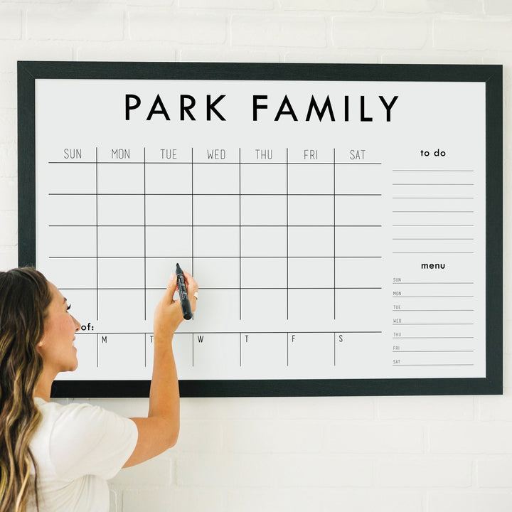 A framed whiteboard weekly calender hanging on the wall