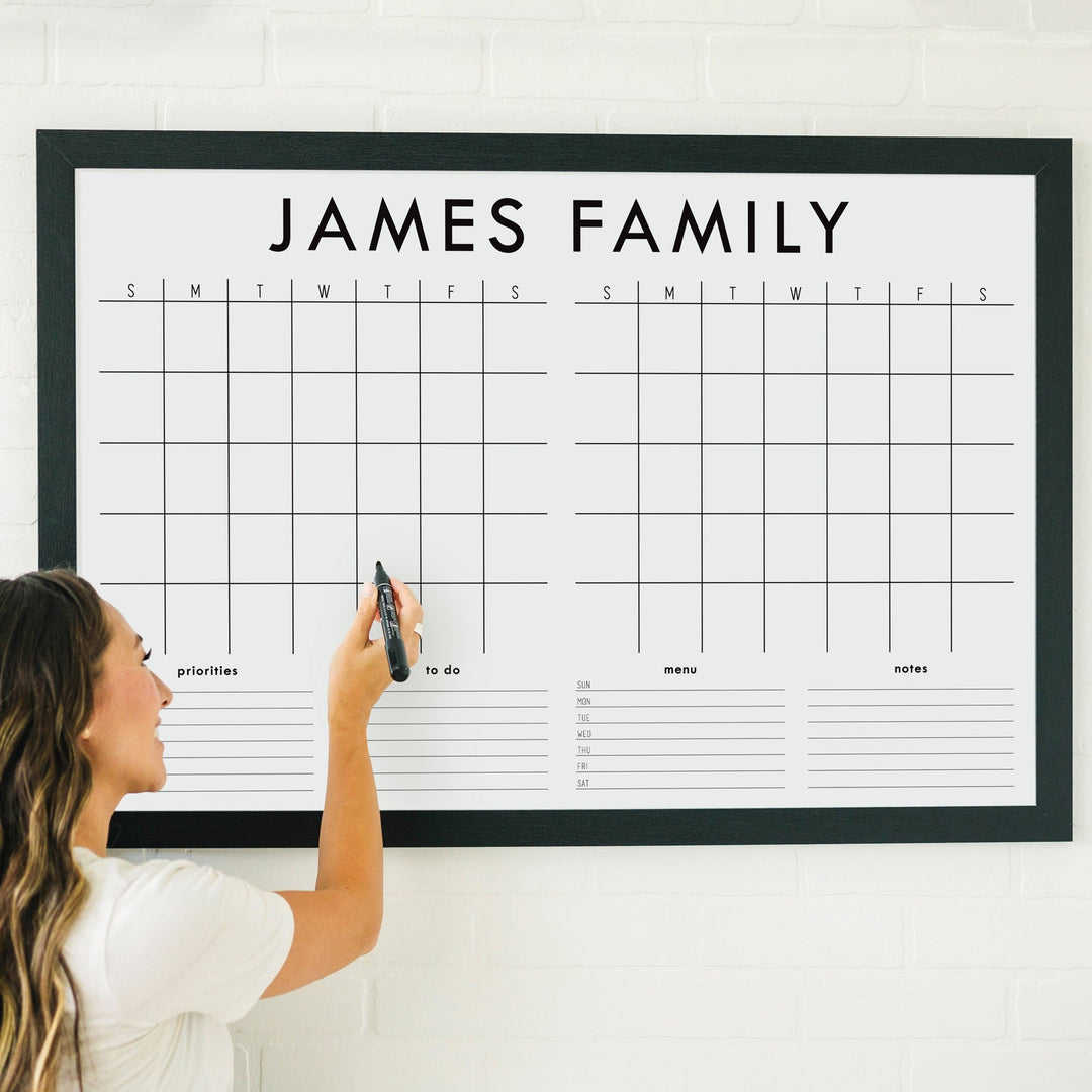 A framed whiteboard calendar with a two month design format hanging on the wall