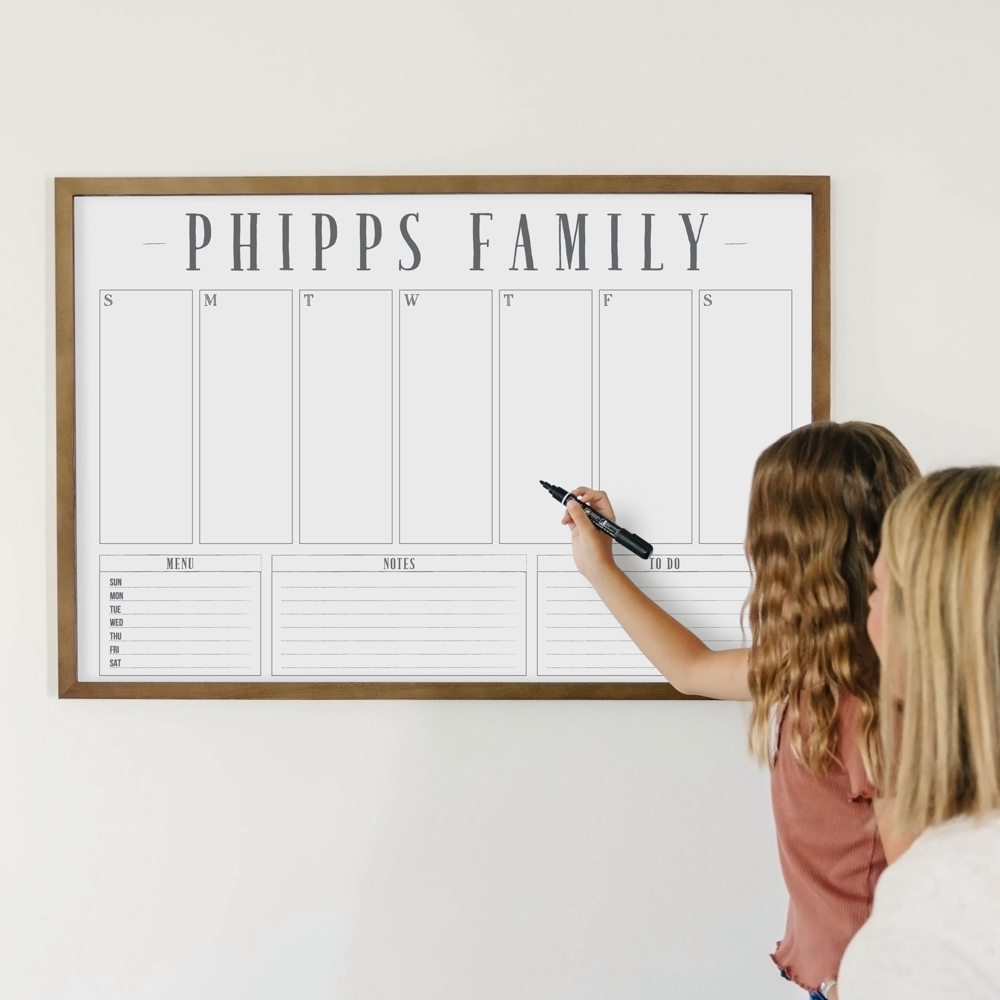 A framed whiteboard weekly calender hanging on the wall