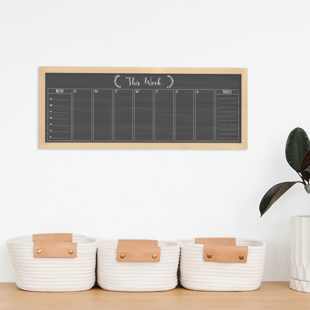 A framed slim dry-erase weekly calender with a faux chalkboard look hanging on the wall