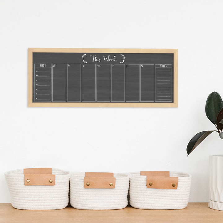 A framed slim dry-erase weekly calender with a faux chalkboard look hanging on the wall