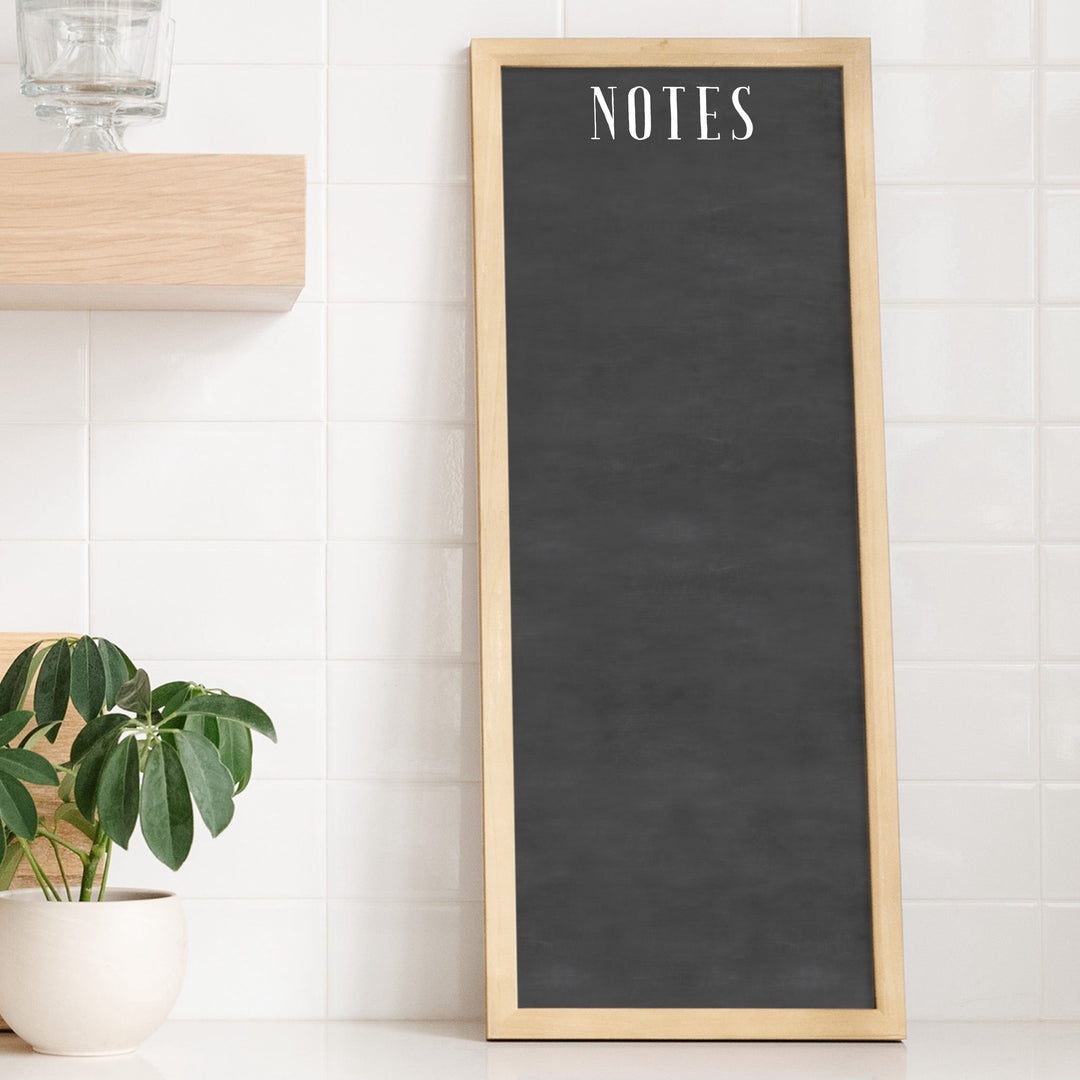 A framed dry-erase chalkboard calendar with a two month design format hanging on the wall