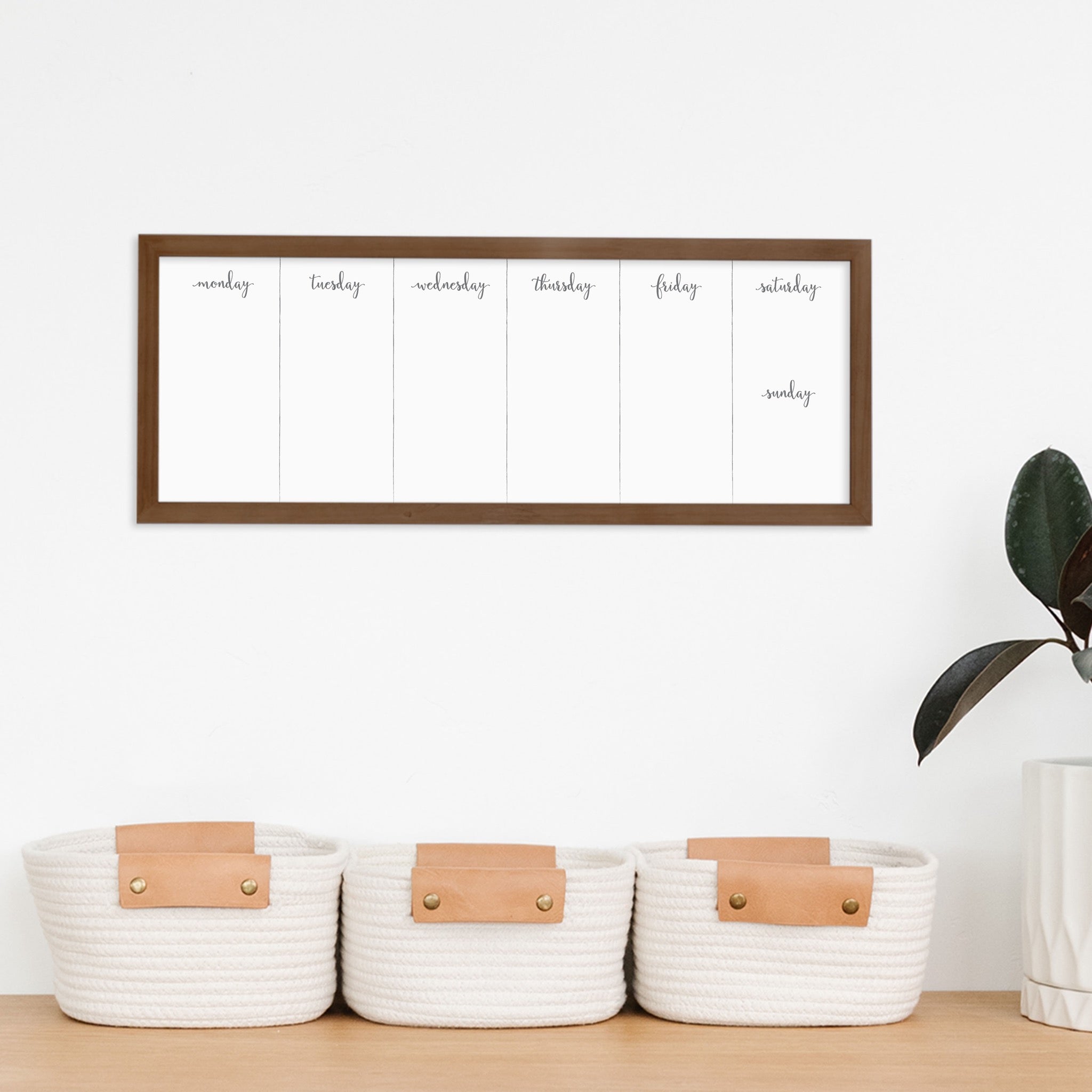 A framed slim whiteboard weekly calender hanging on the wall