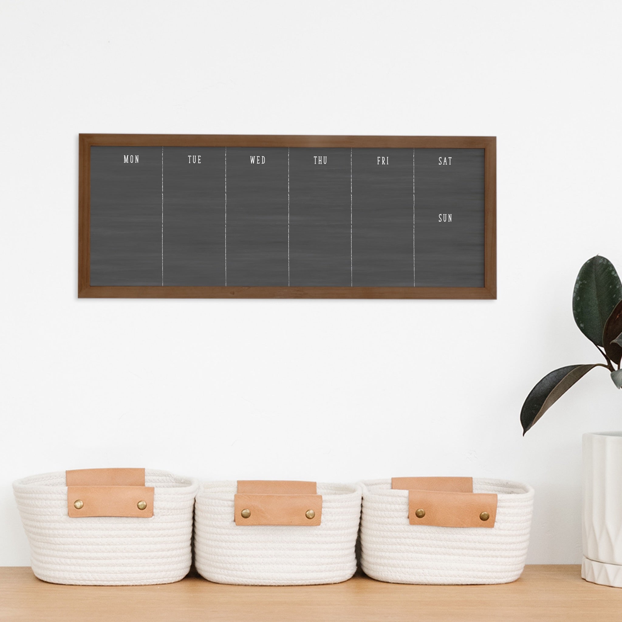 A framed slim dry-erase weekly calender with a faux chalkboard look hanging on the wall
