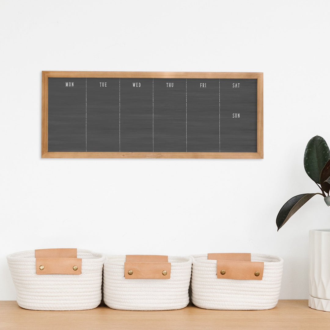 A framed slim dry-erase weekly calender with a faux chalkboard look hanging on the wall