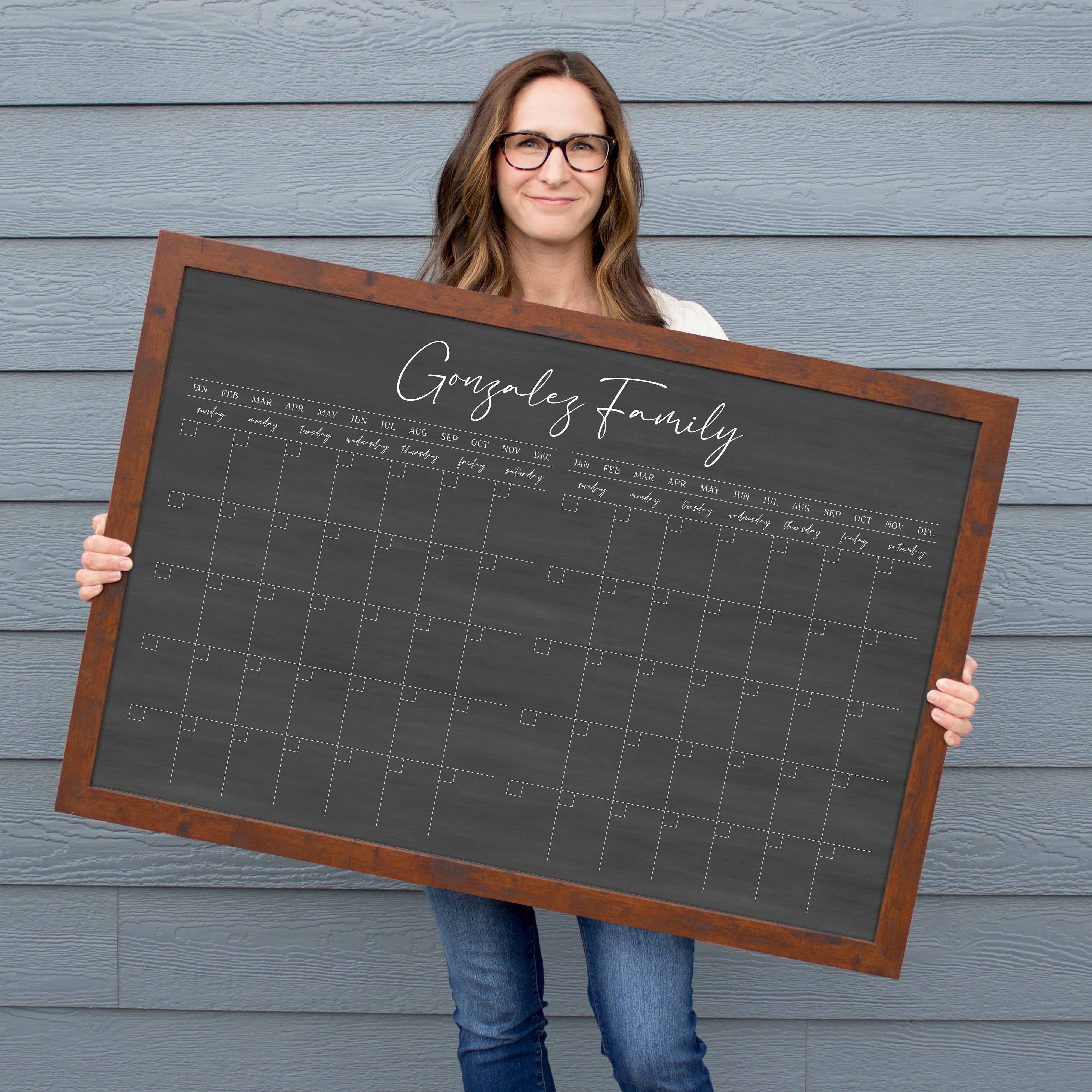 A framed chalkboard dry-erase calendar with a two month design format hanging on the wall