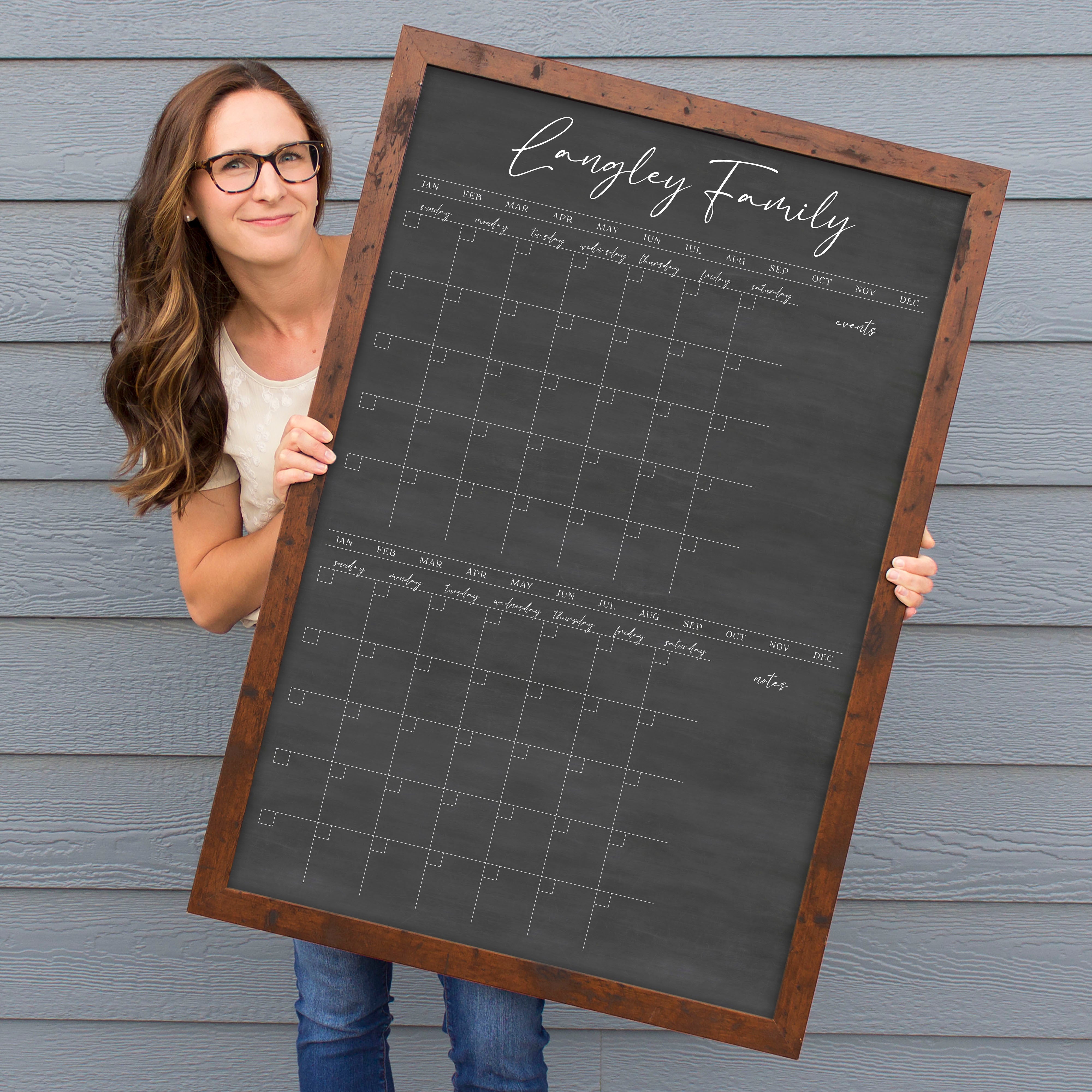 A framed chalkboard dry-erase calendar with a two month design format hanging on the wall