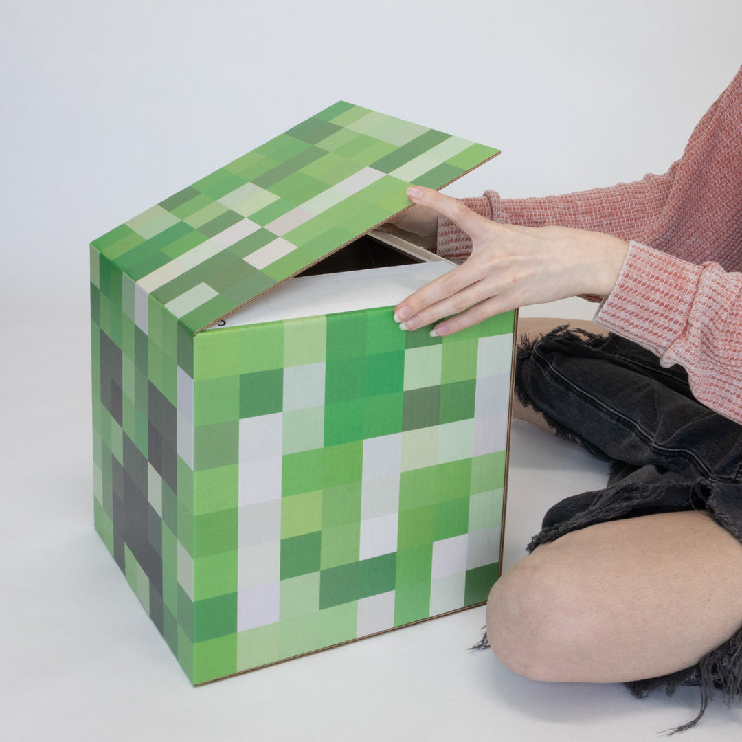 A person folding up a creeper head pixel cube.
