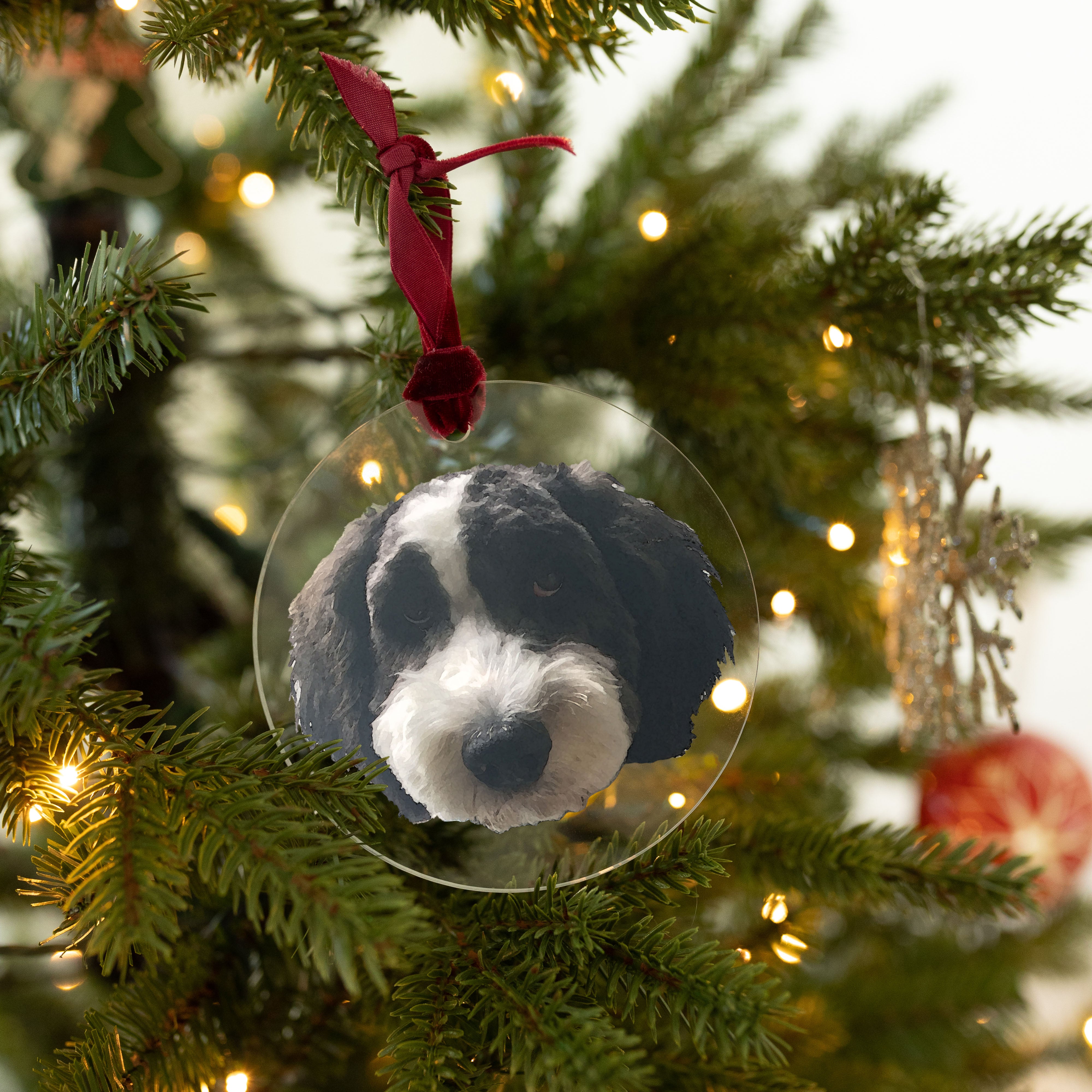 A dog ornament hanging on a Christmas tree with a dark red ribbon. The dog's face is printed on a 4x4" acrylic circle.