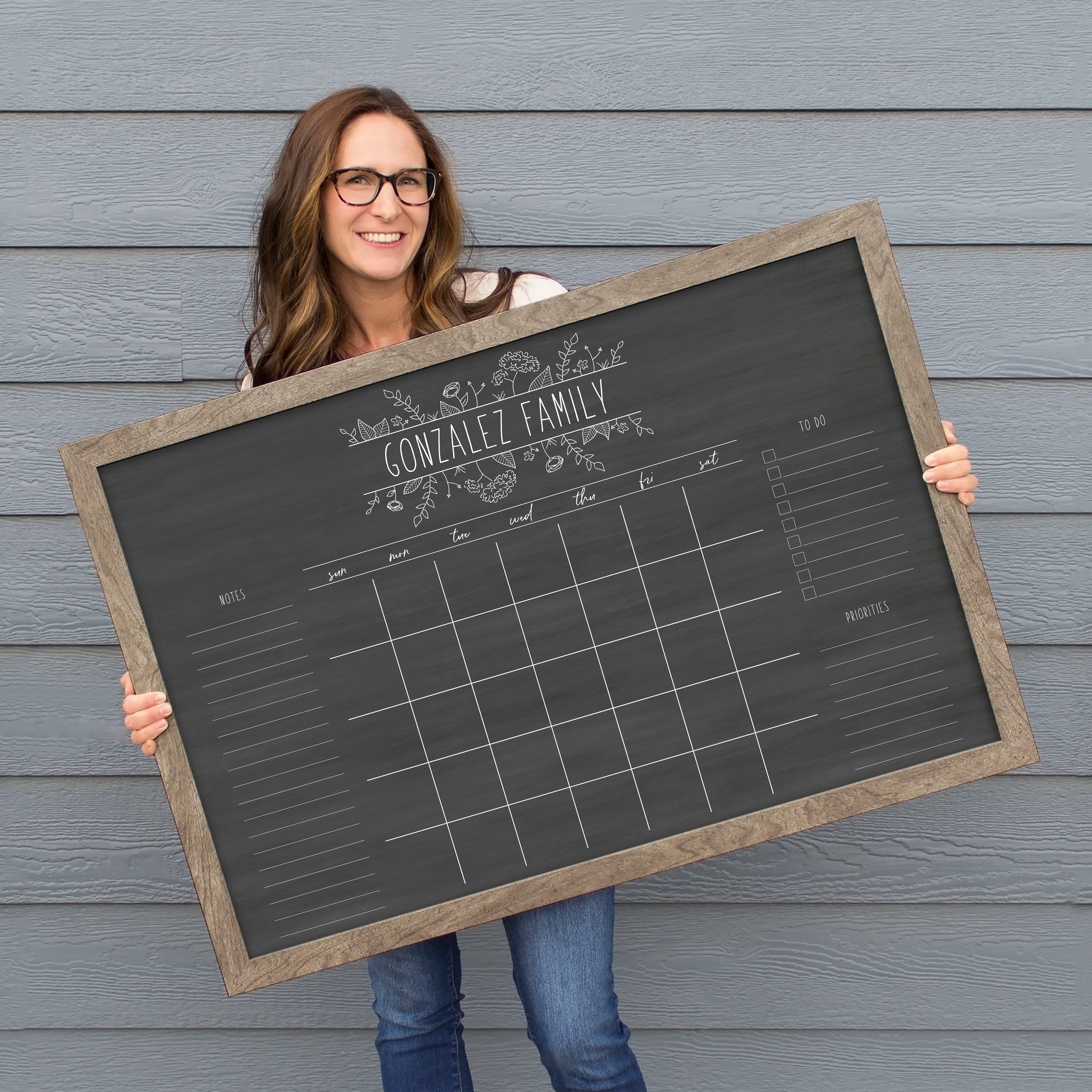 A framed dry-erase monthly calender with a chalkboard look hanging on the wall