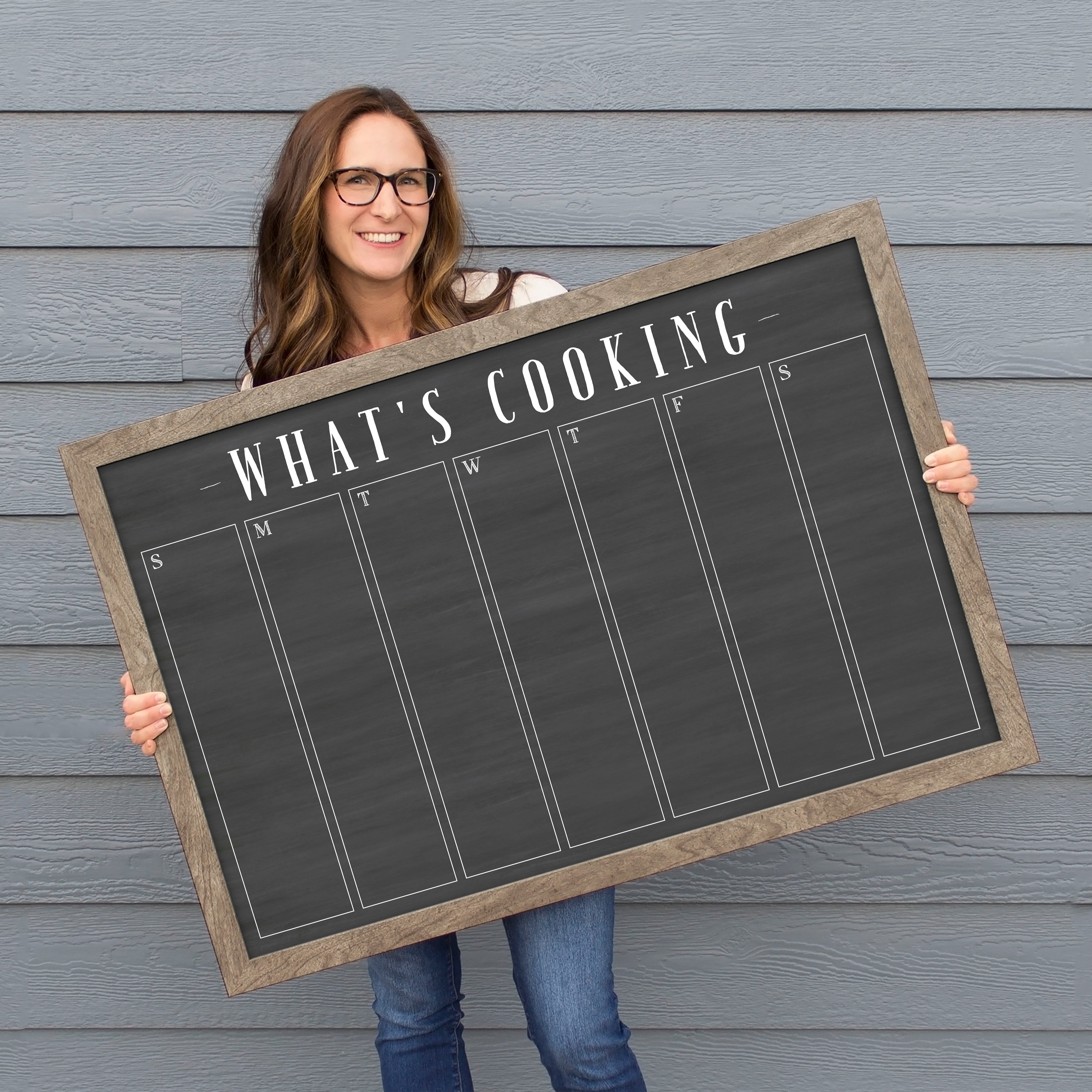 A framed dry-erase weekly calender with a chalkboard look hanging on the wall