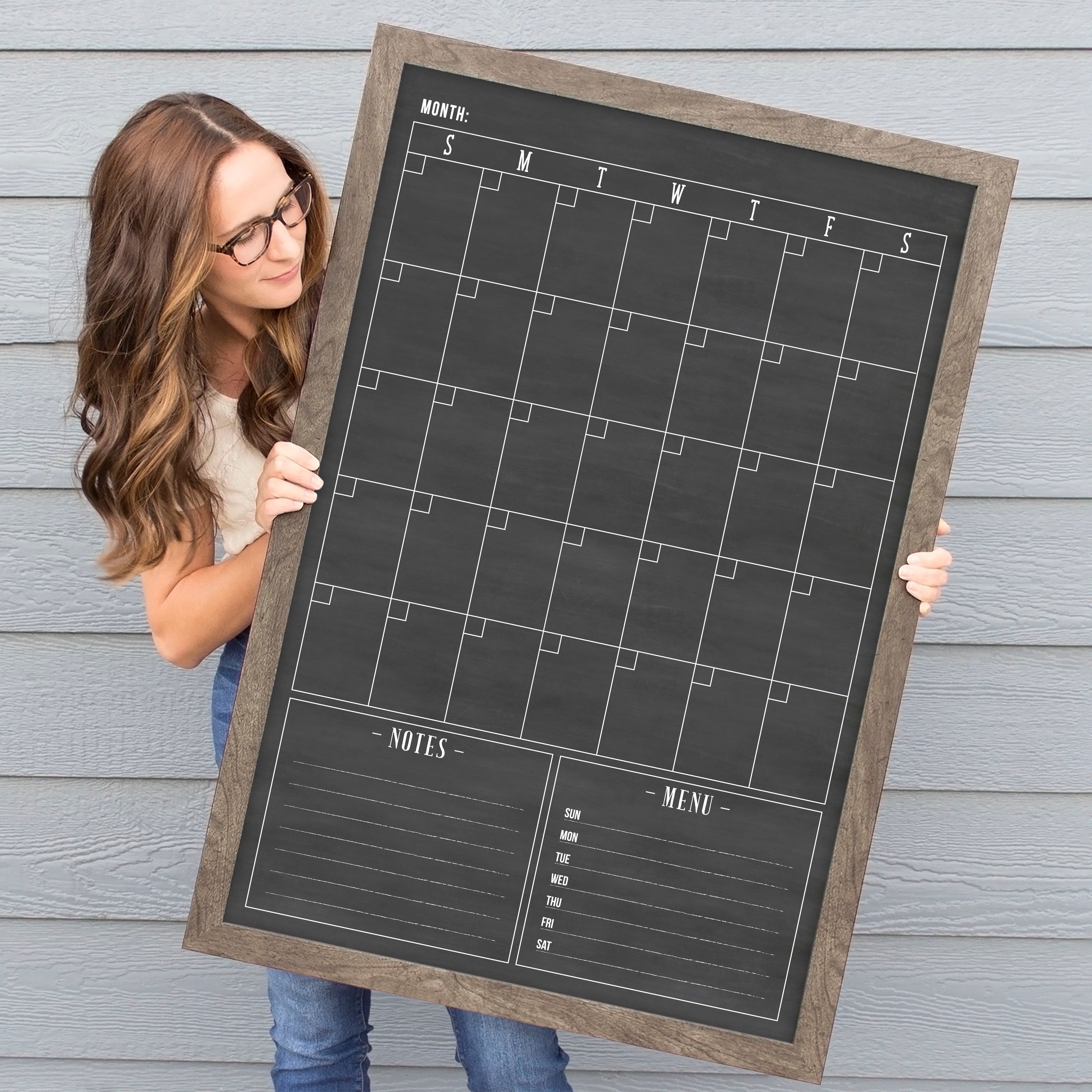 A framed dry-erase monthly calender with a chalkboard look hanging on the wall