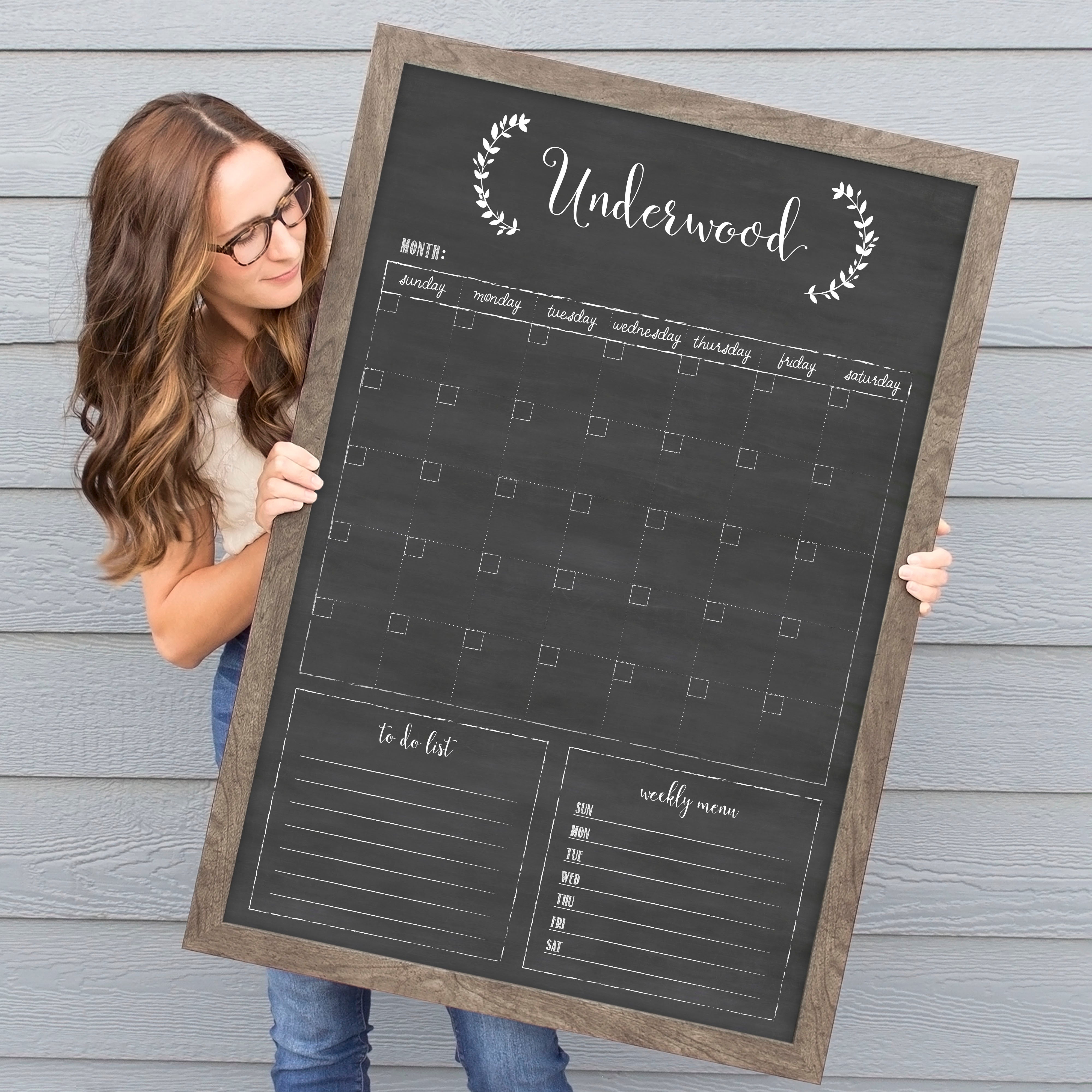 A framed dry-erase monthly calender with a chalkboard look hanging on the wall