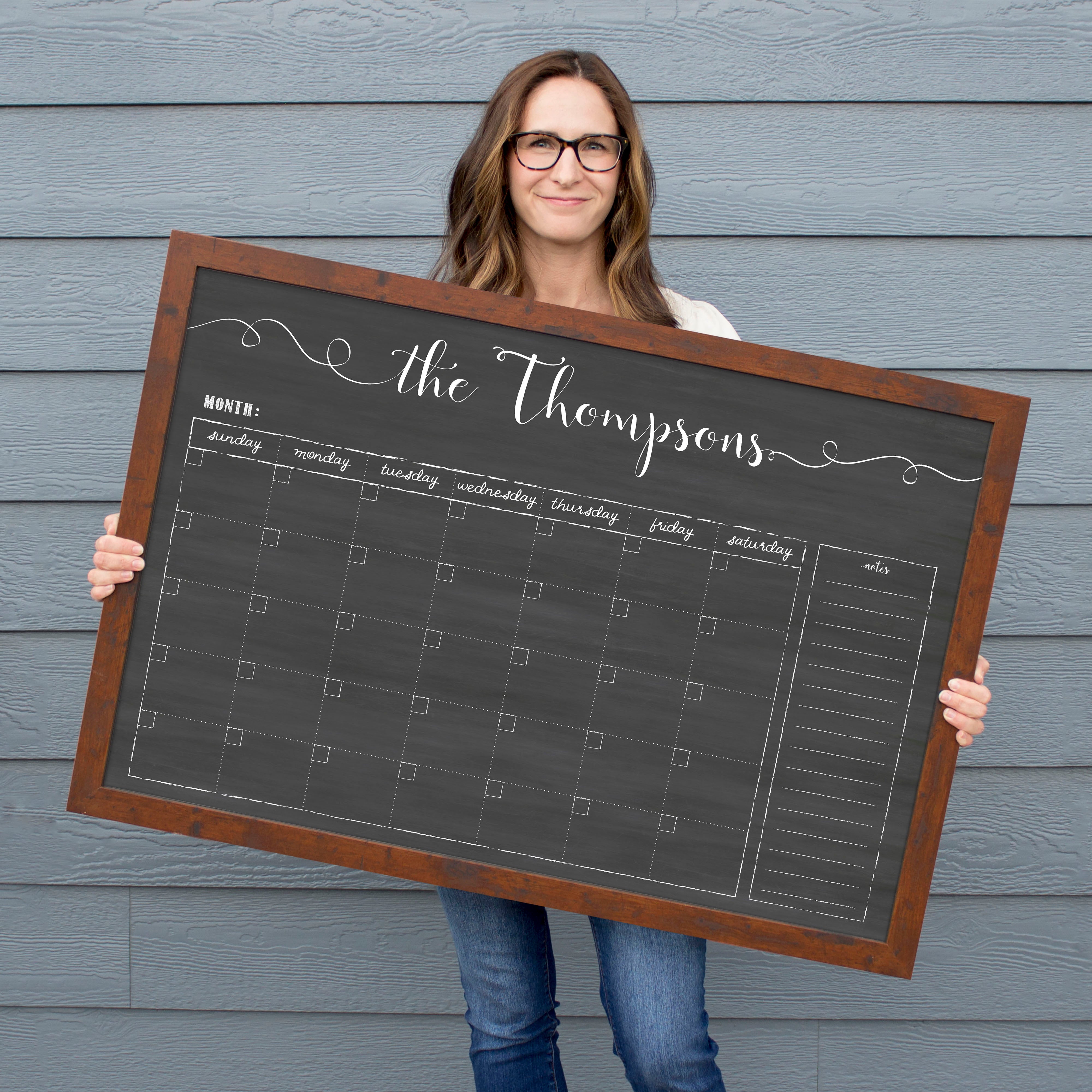 A framed dry-erase monthly calender with a chalkboard look hanging on the wall