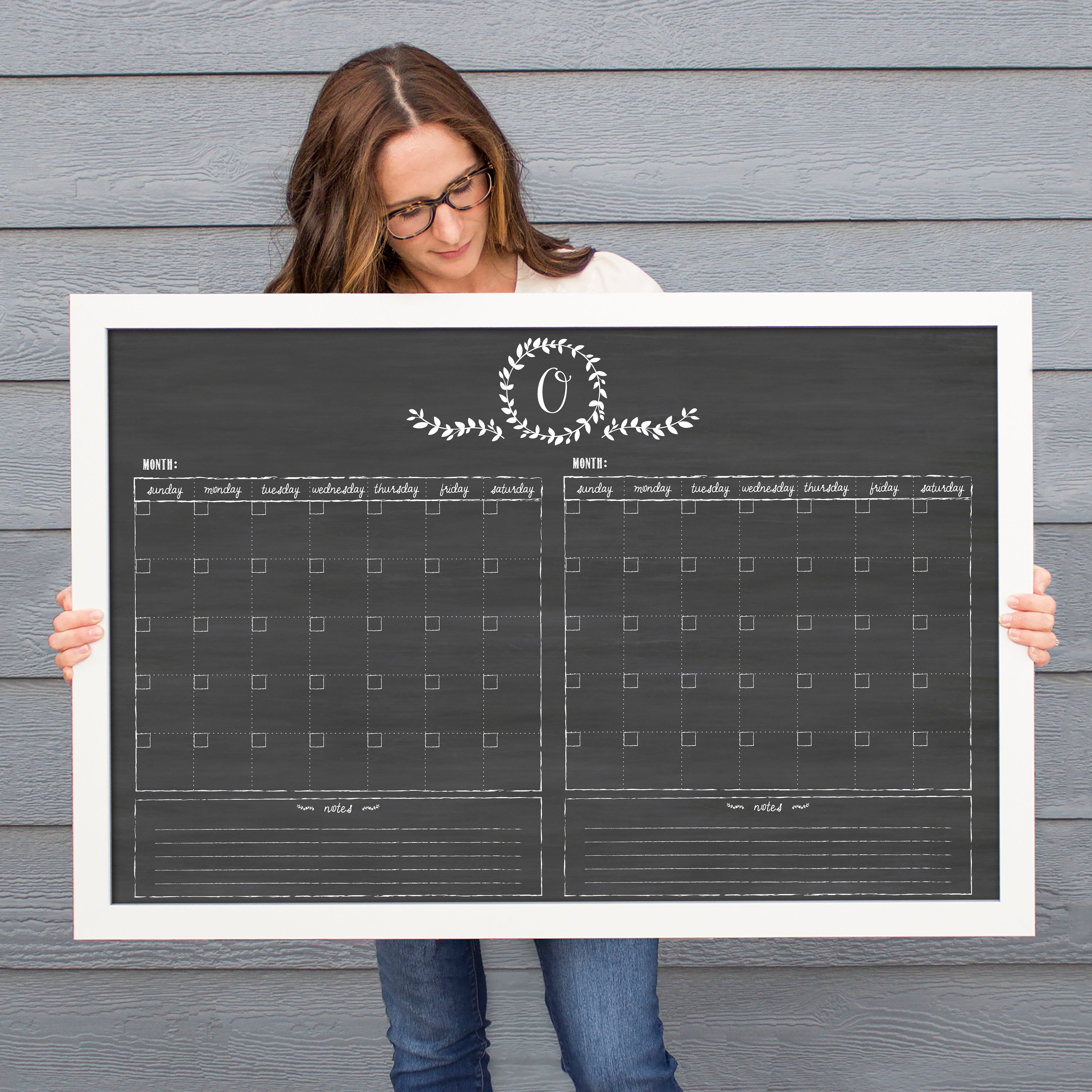 A framed chalkboard dry-erase calendar with a two month design format hanging on the wall