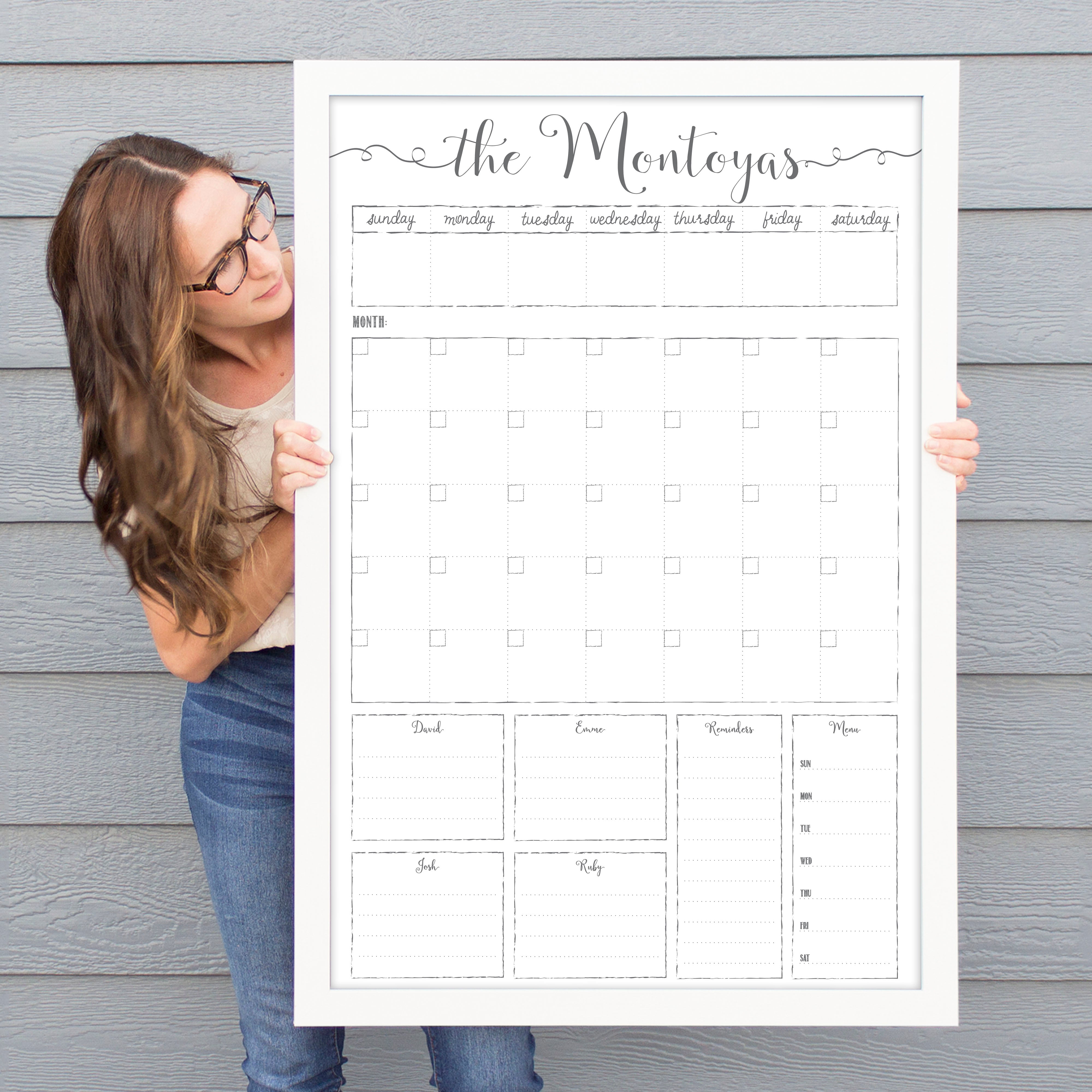 A framed whiteboard calendar with a monthly and weekly format hanging on the wall