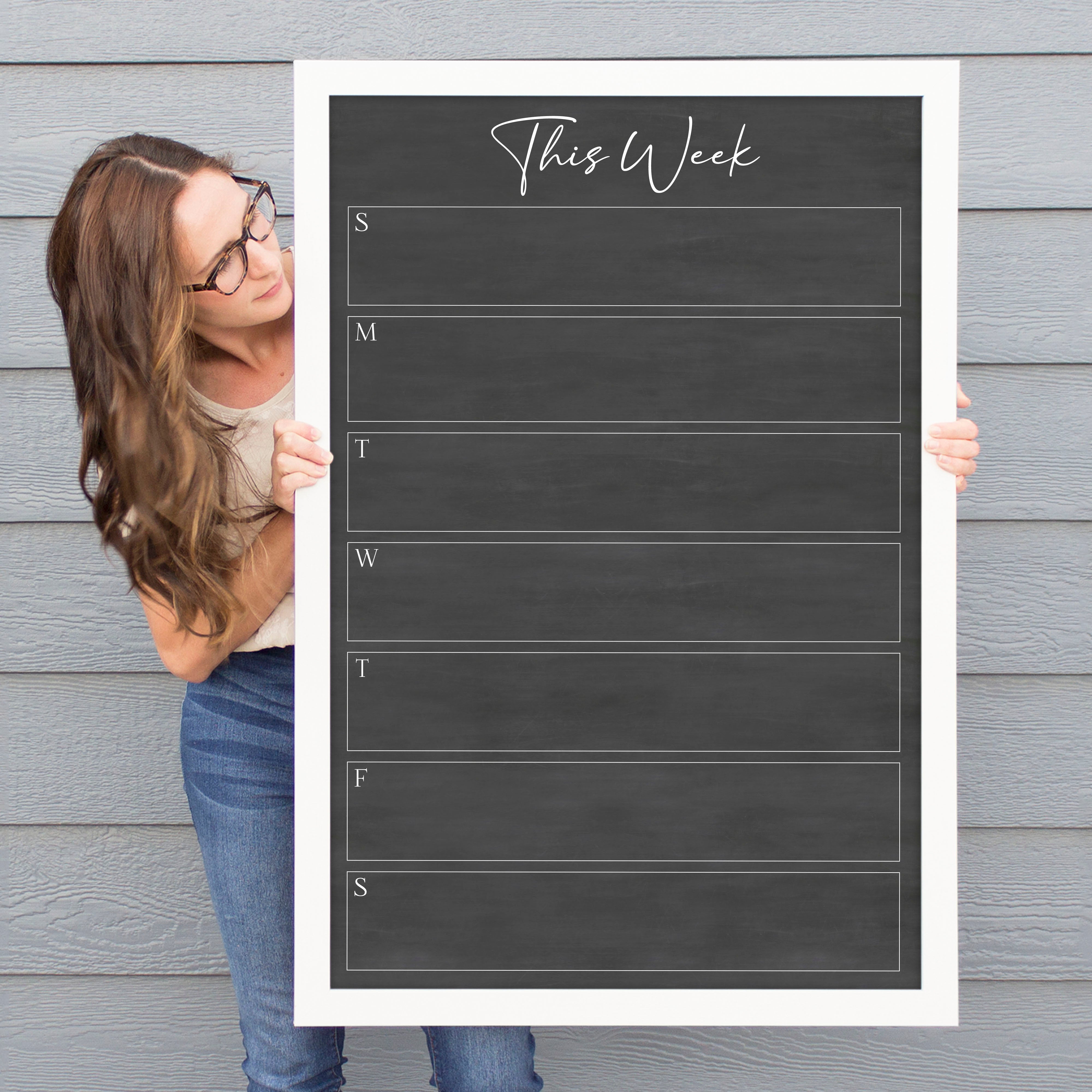 A framed dry-erase weekly calender with a chalkboard look hanging on the wall