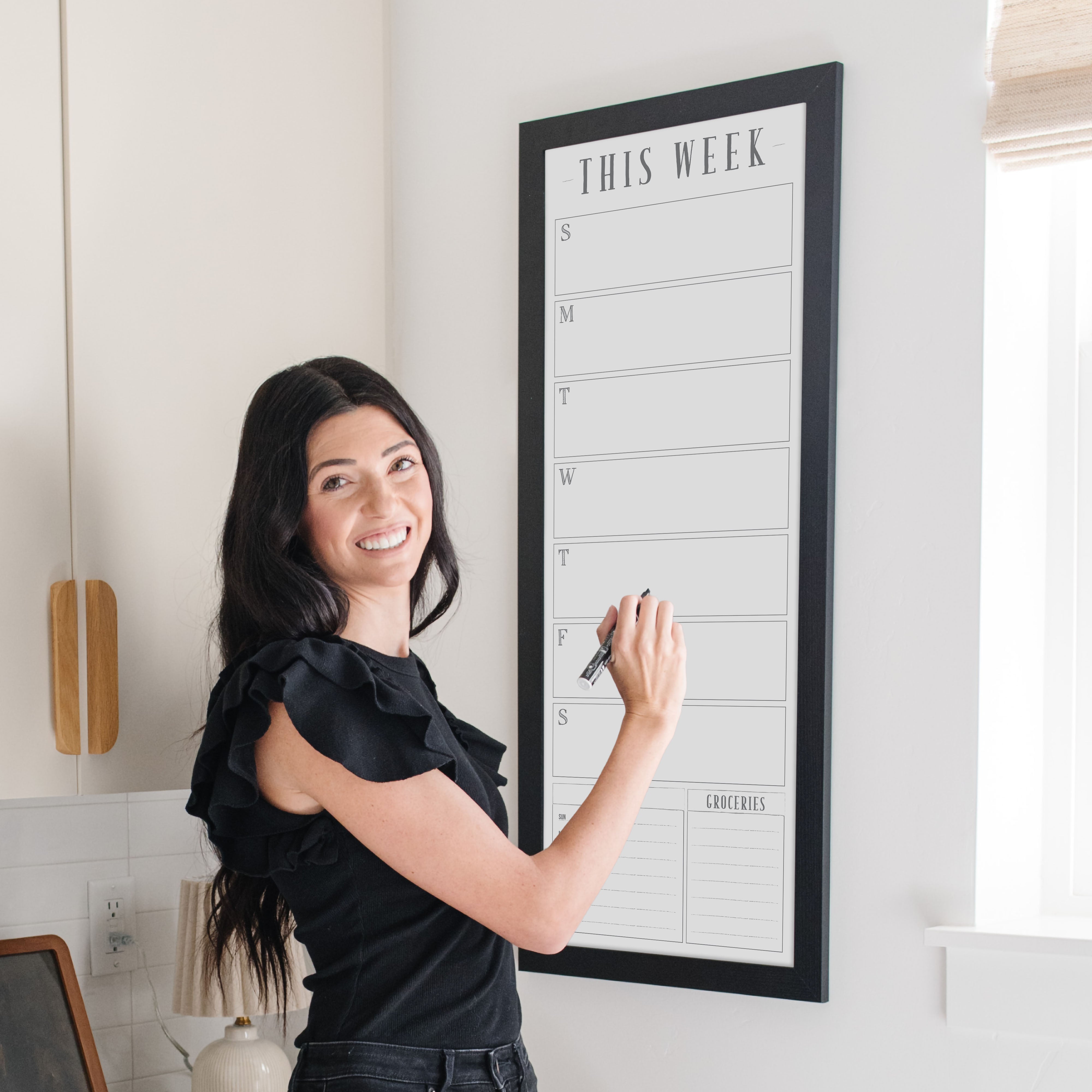 A framed slim whiteboard weekly calender hanging on the wall