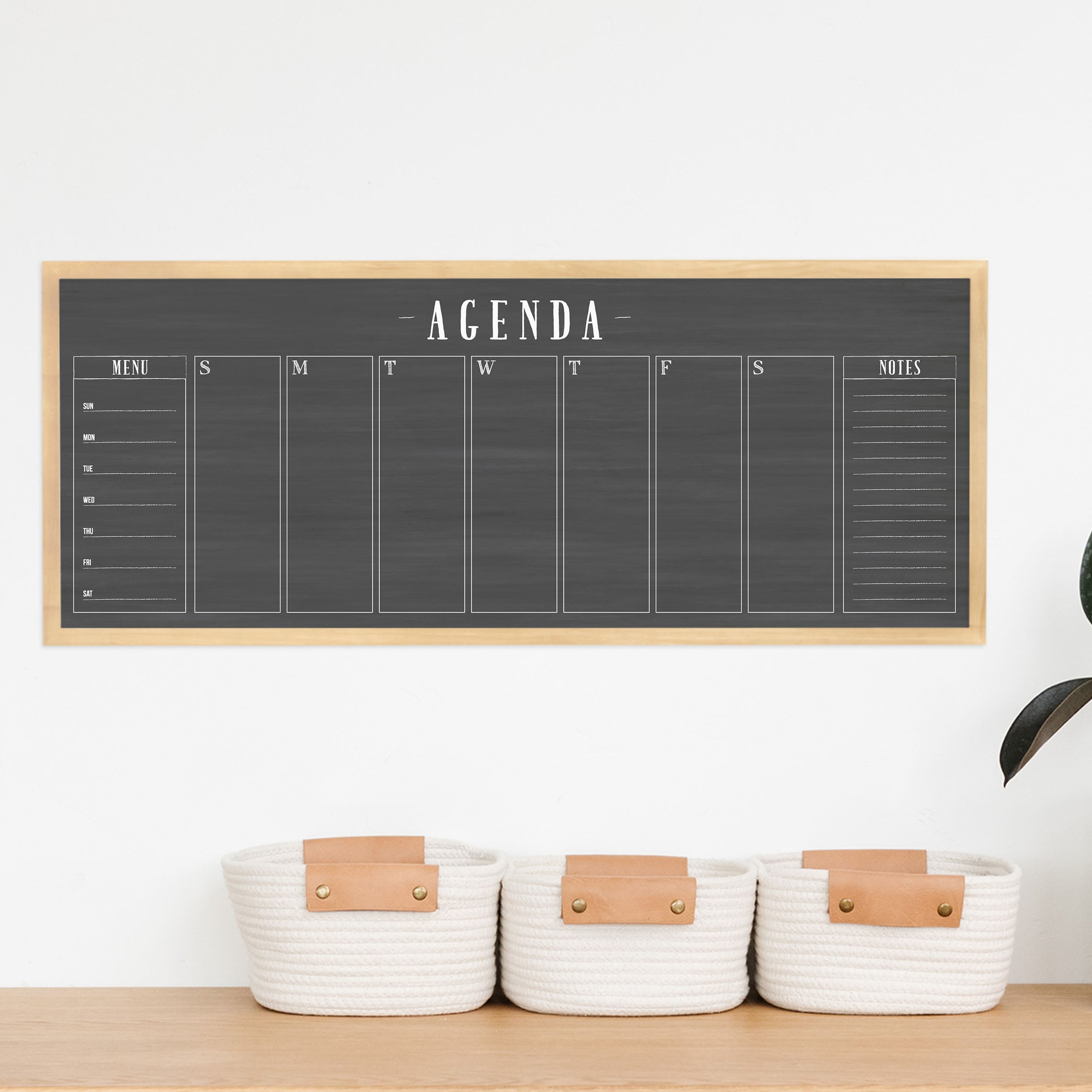 A framed slim dry-erase weekly calender with a faux chalkboard look hanging on the wall