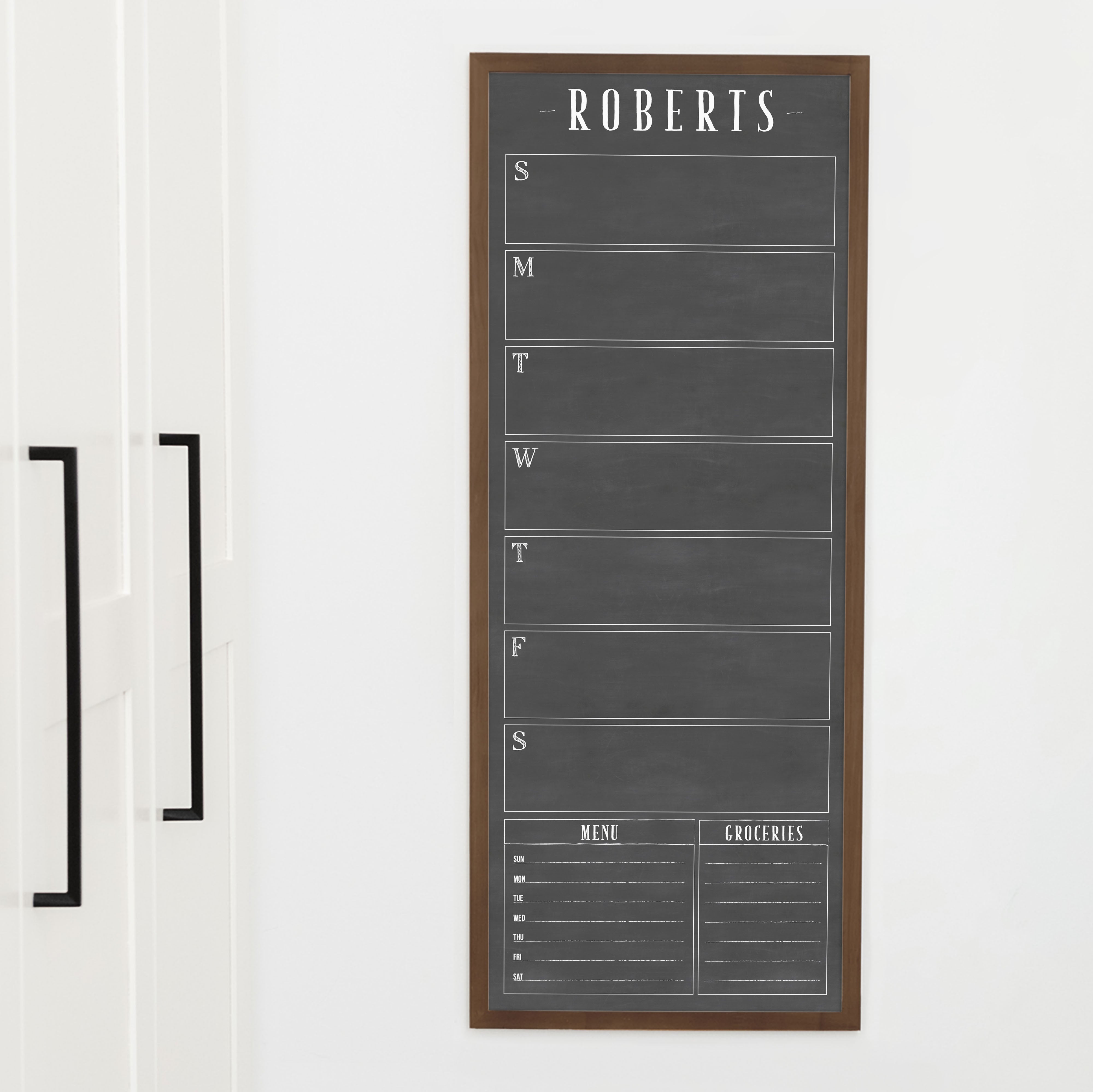 A framed slim dry-erase weekly calender with a faux chalkboard look hanging on the wall